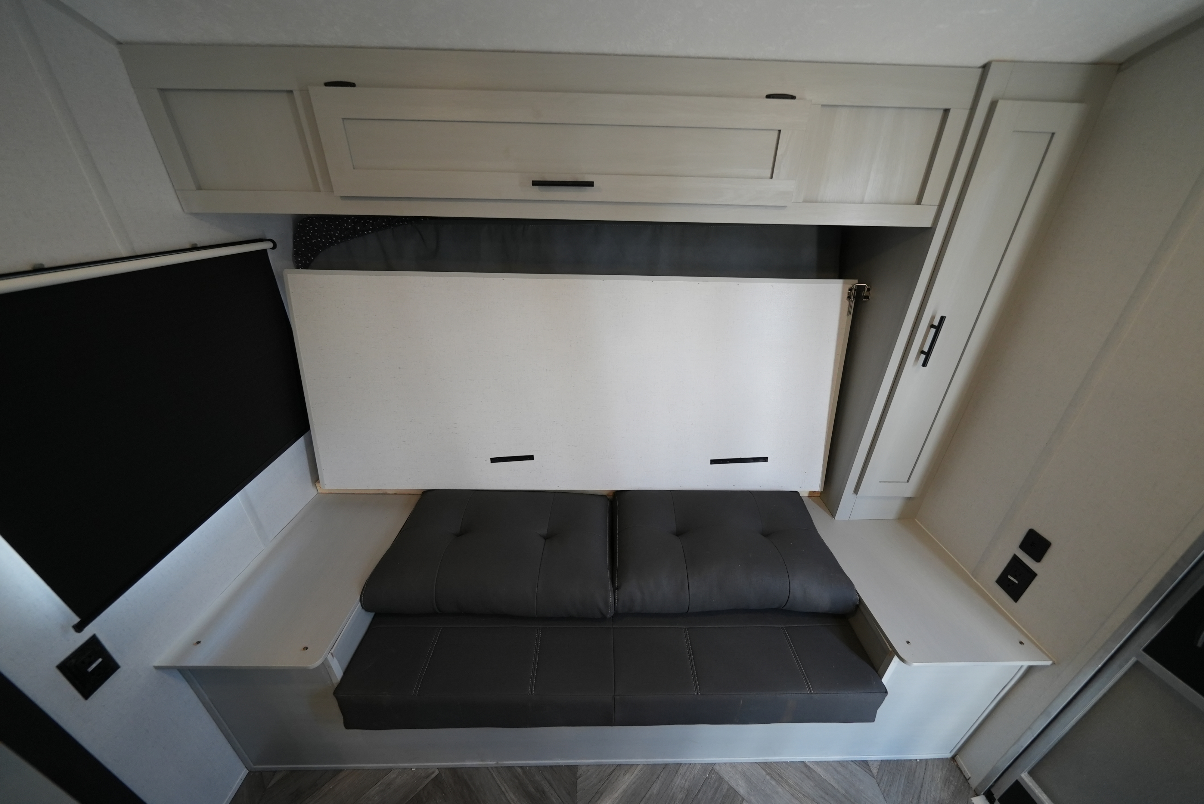 RV rental interior featuring a clever murphy bed setup with a gray sofa and overhead cabinets, maximizing space.. Forest River Wildwood FSX 2022