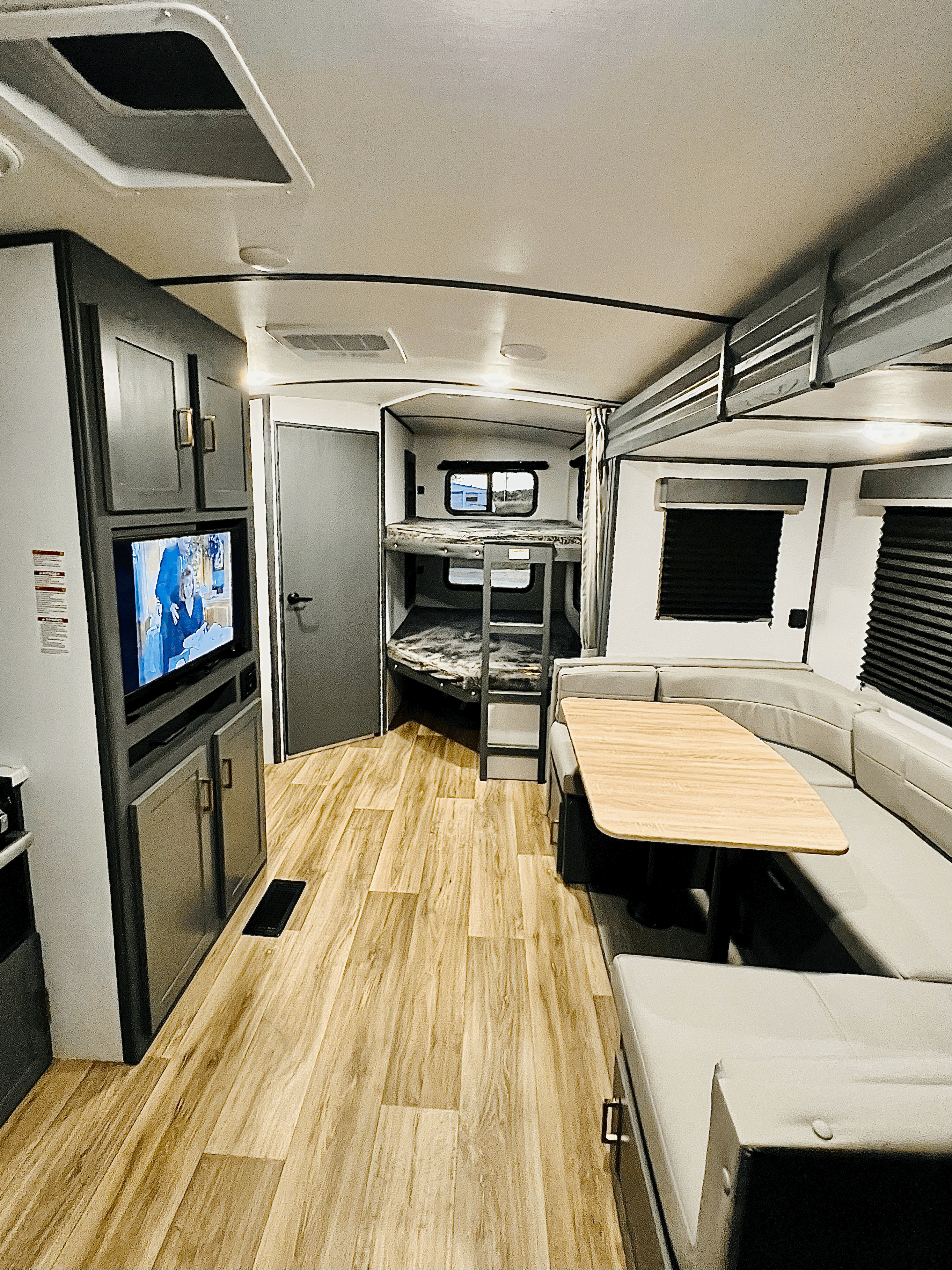 Spacious RV rental interior: a bright living area with a U-shaped dinette, TV, and bunk beds, featuring wood-look flooring.. Keystone Bullet 250BHS 2022