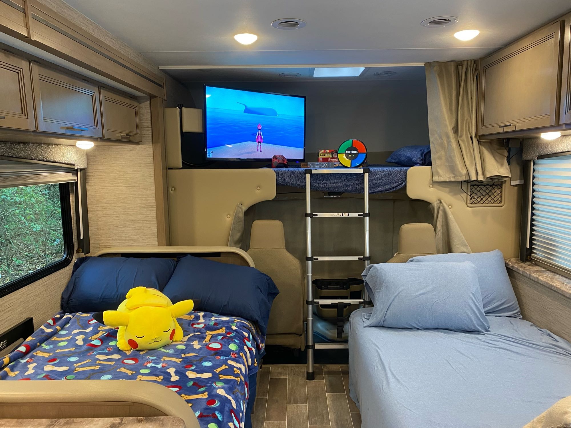 Cozy RV rental interior featuring a TV, bunk beds, and two single beds, one with a Pikachu plush.. Thor Magnitude GA 2022