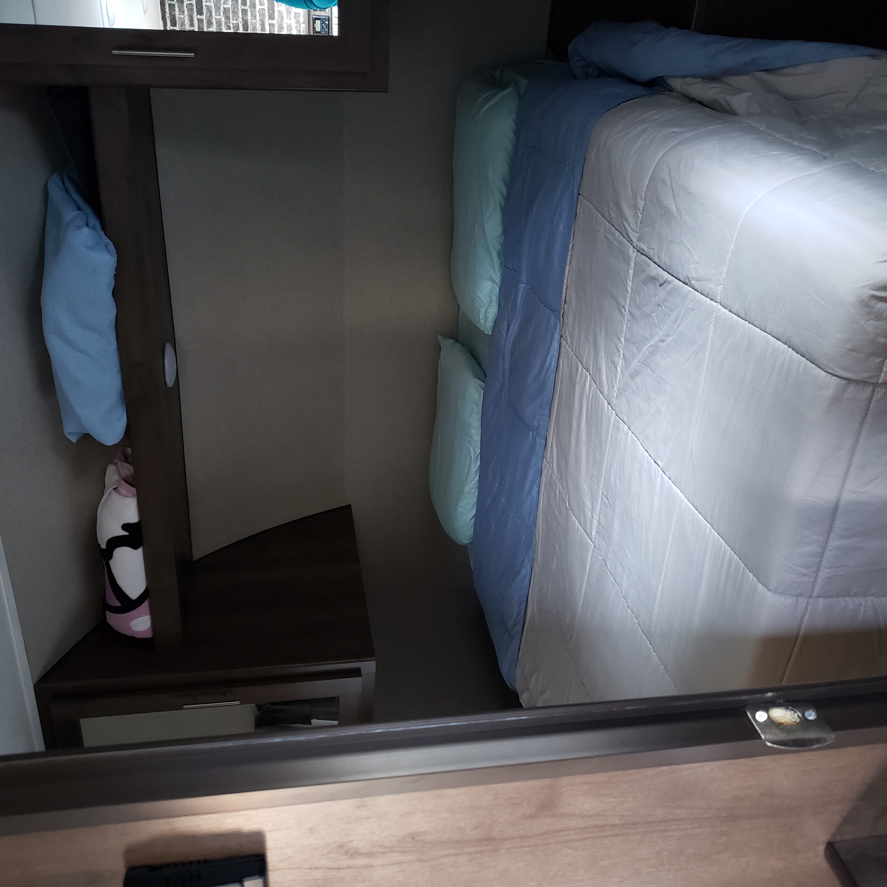 RV rental bedroom with a cozy bed featuring blue and white bedding, alongside a compact storage cabinet with hanging items.. Forest River Shasta 2020