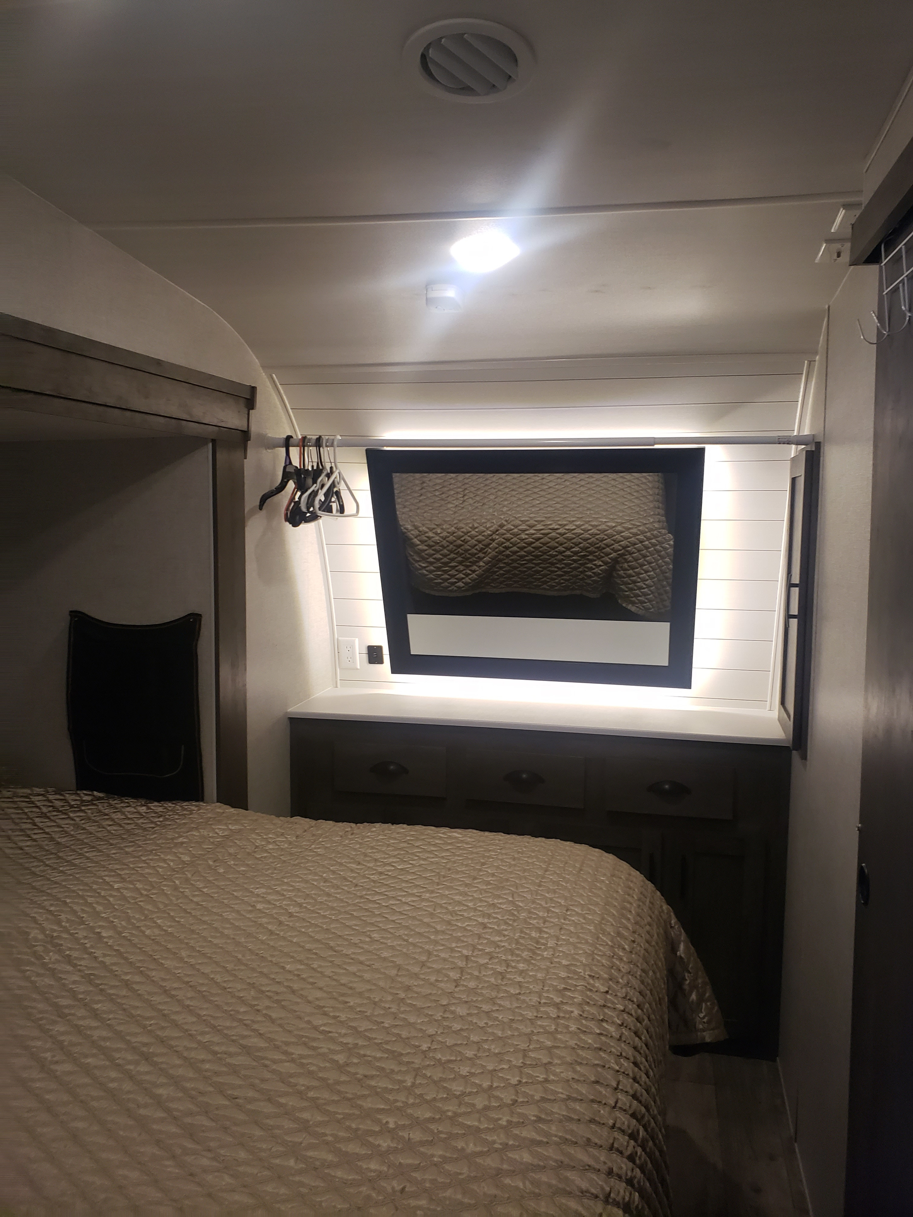 Explore this modern RV rental bedroom featuring a comfy bed, built-in storage, and illuminated vanity mirror.. Forest River Shockwave 2021