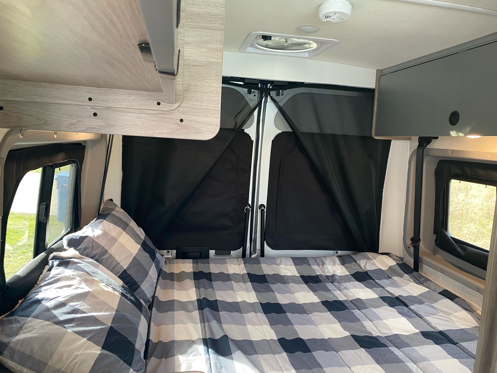 Cozy plaid bed in this RV rental, showcasing clever storage, window shades, and a ceiling vent for comfort.. Winnebago Solis 2022
