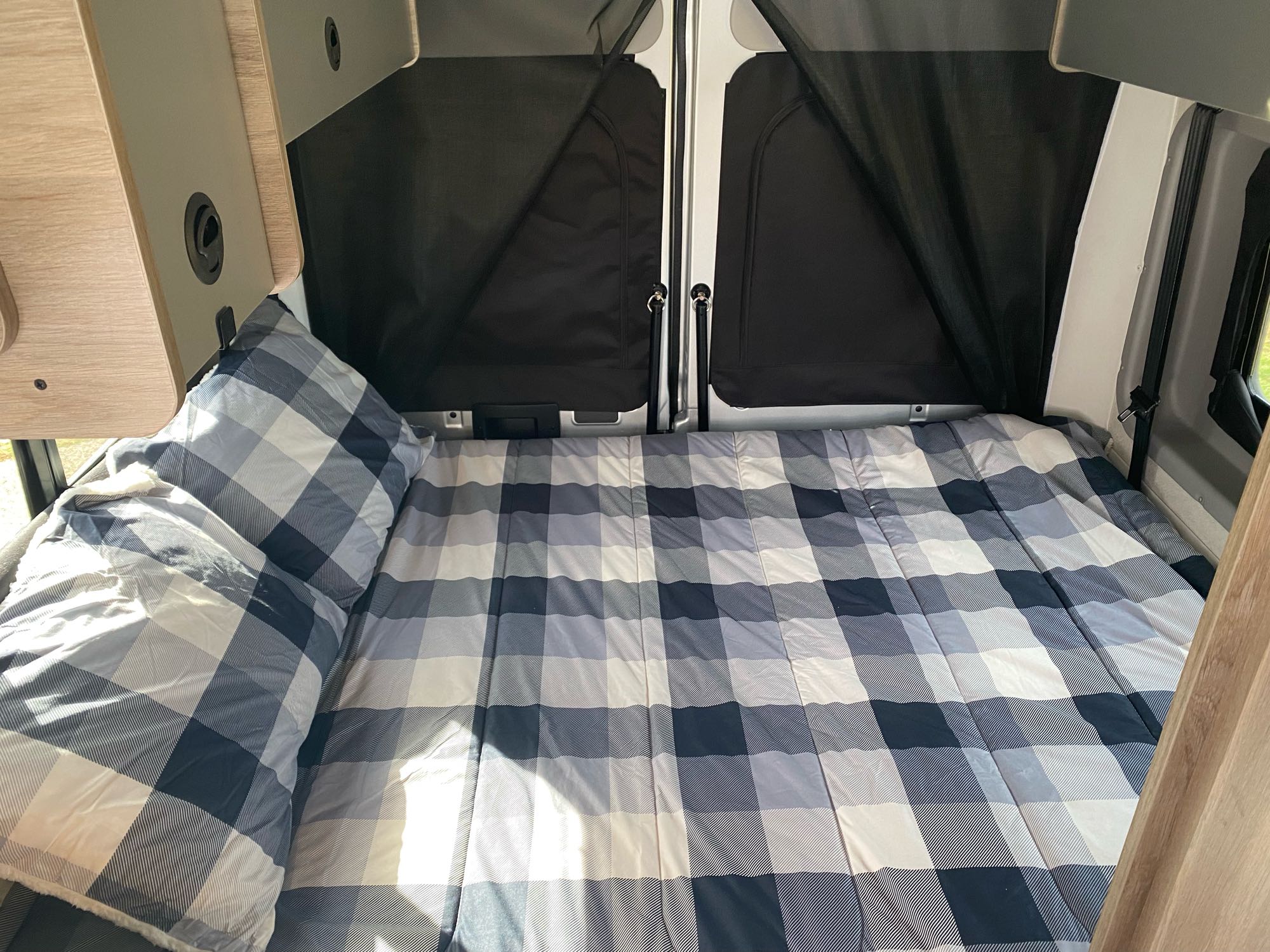 Cozy bed in an RV rental with blue, white, and grey plaid bedding & black privacy shades. Perfect for a road trip.. Winnebago Solis 2022