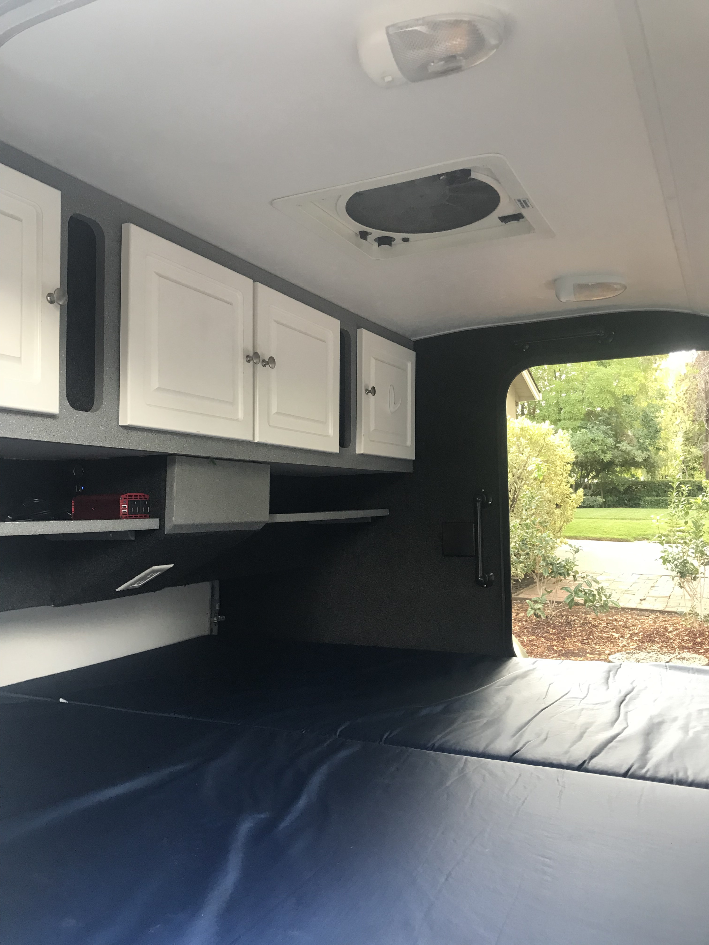 Spacious RV rental interior with white overhead storage, a blue bed, ceiling fan, and outdoor view from the rear.. Little Guy Other 2011