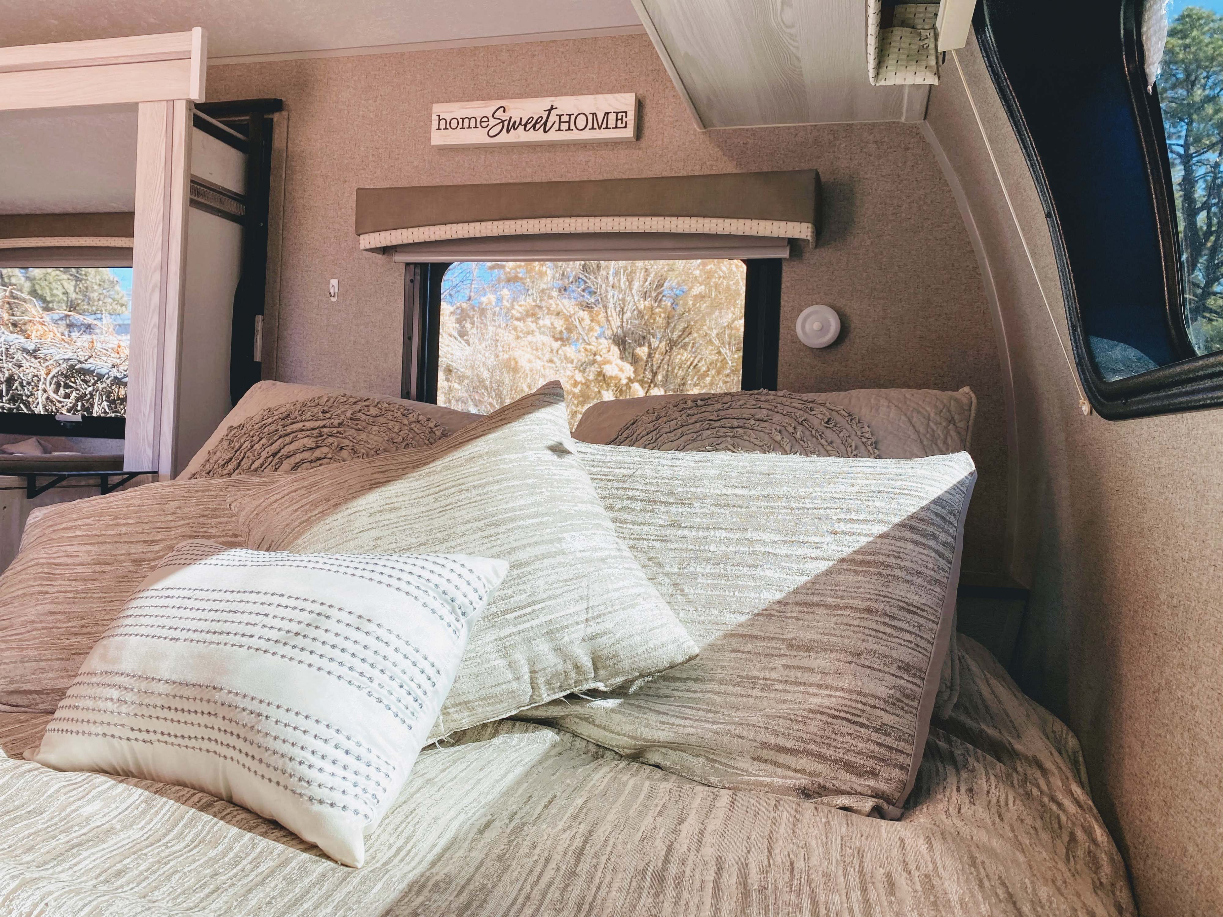 Cozy RV rental bedroom with plush pillows, 'home Sweet HOME' decor, and a window view of outdoor nature.. Forest River Rockwood 2021