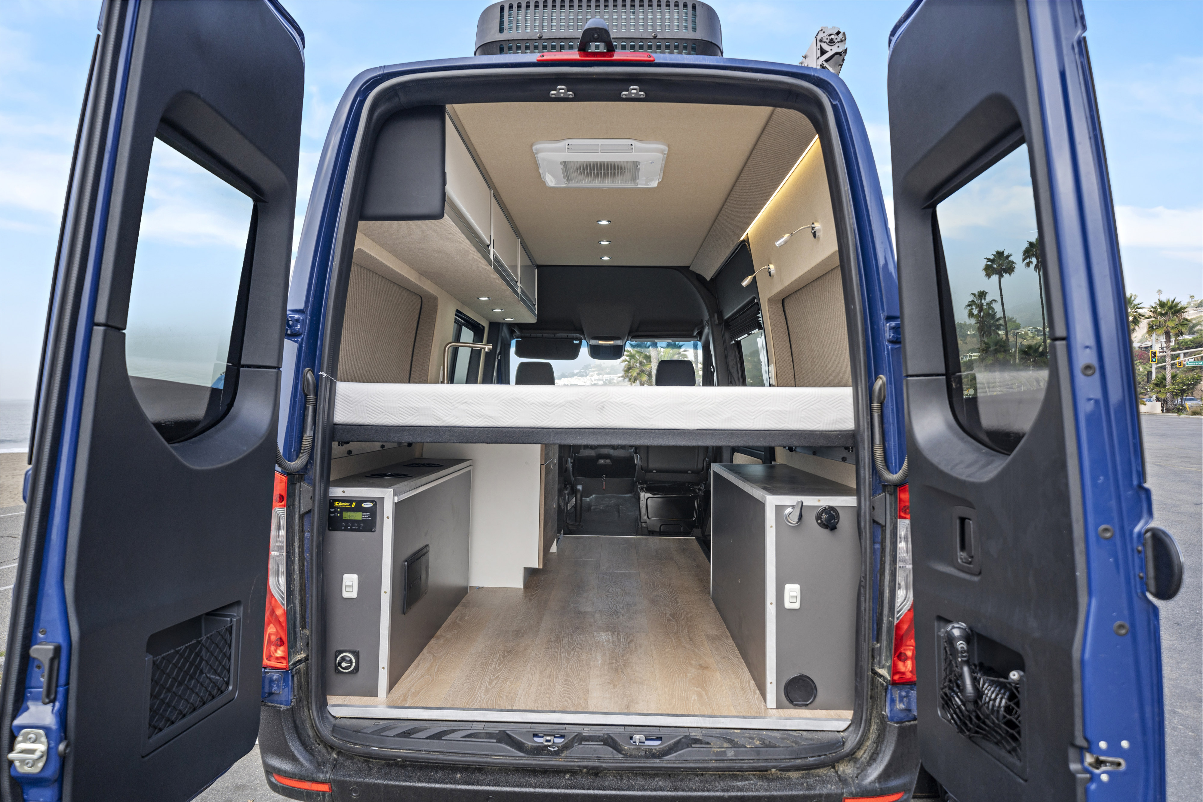 Rear view of an RV rental with open doors, revealing a spacious camper van interior featuring a bed, kitchen, & storage.. Mercedes Sprinter 2021