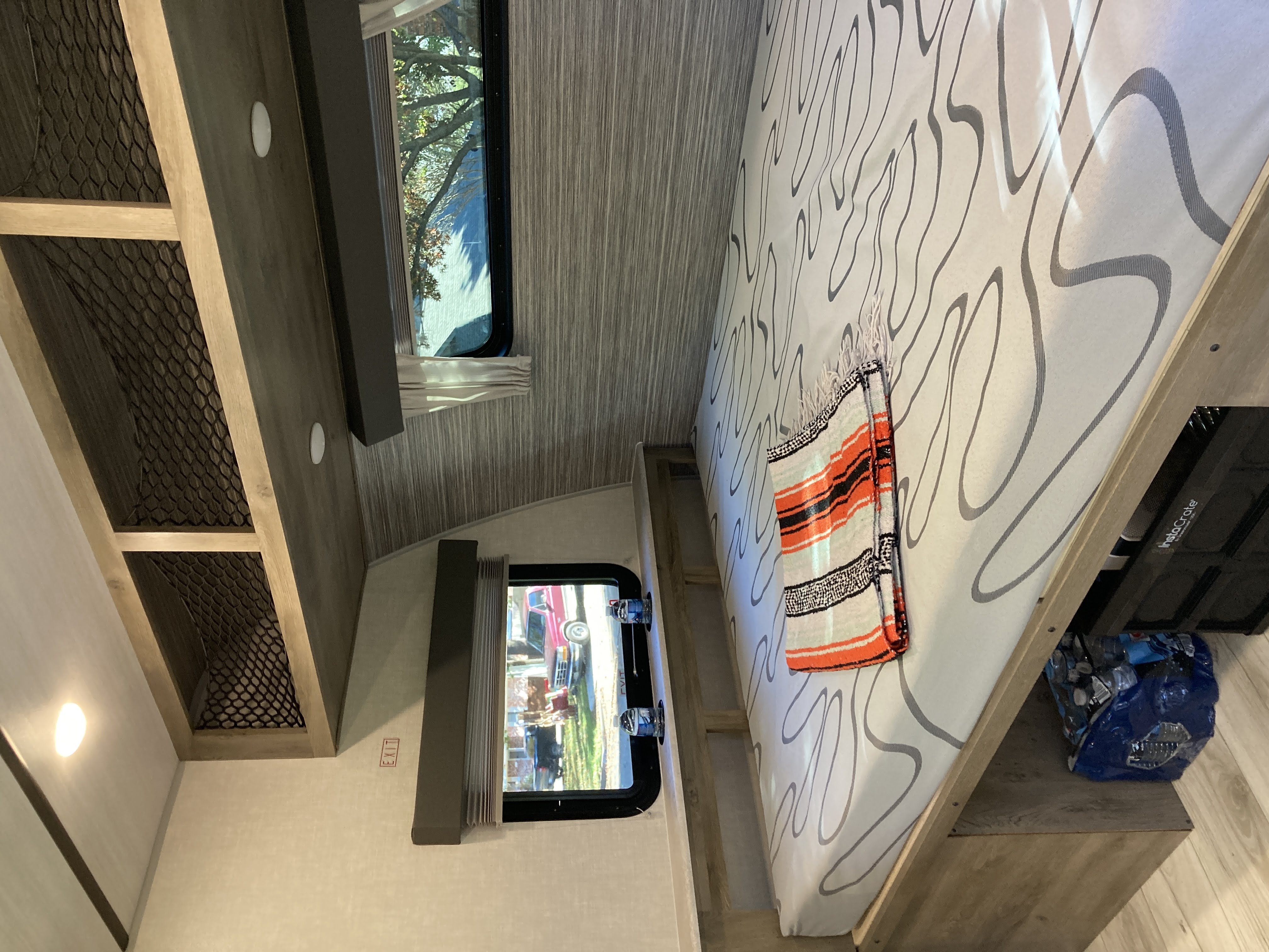 RV rental bedroom shows patterned bed, mesh overhead storage, two windows with outdoor views, and under-bed items.. Forest River Surveyor Legend 19BHLE 2022