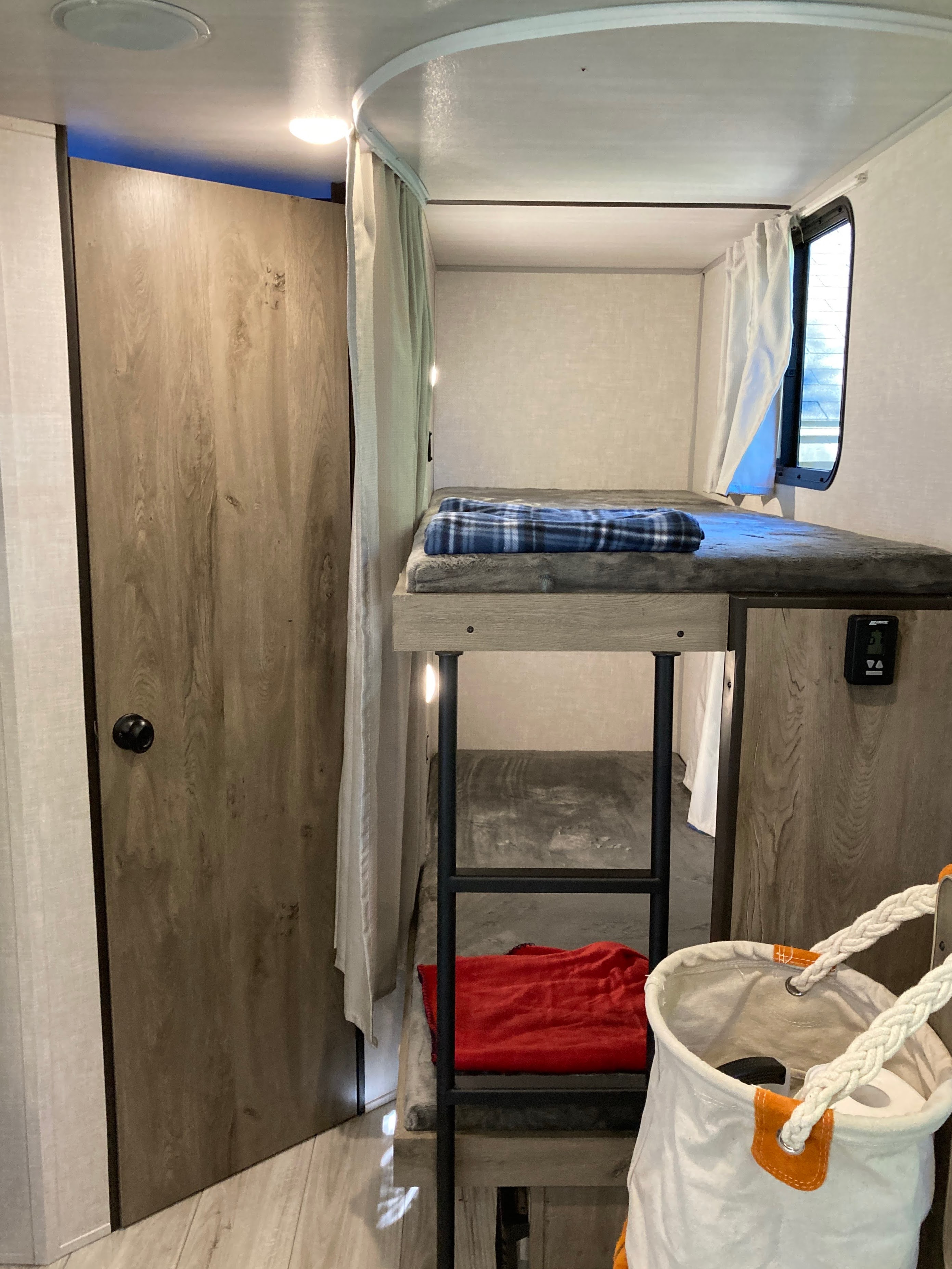 Inside this RV rental: a compact bunk bed with a blue blanket, a wooden door, and privacy curtains for comfortable mobile living.. Forest River Surveyor Legend 19BHLE 2022