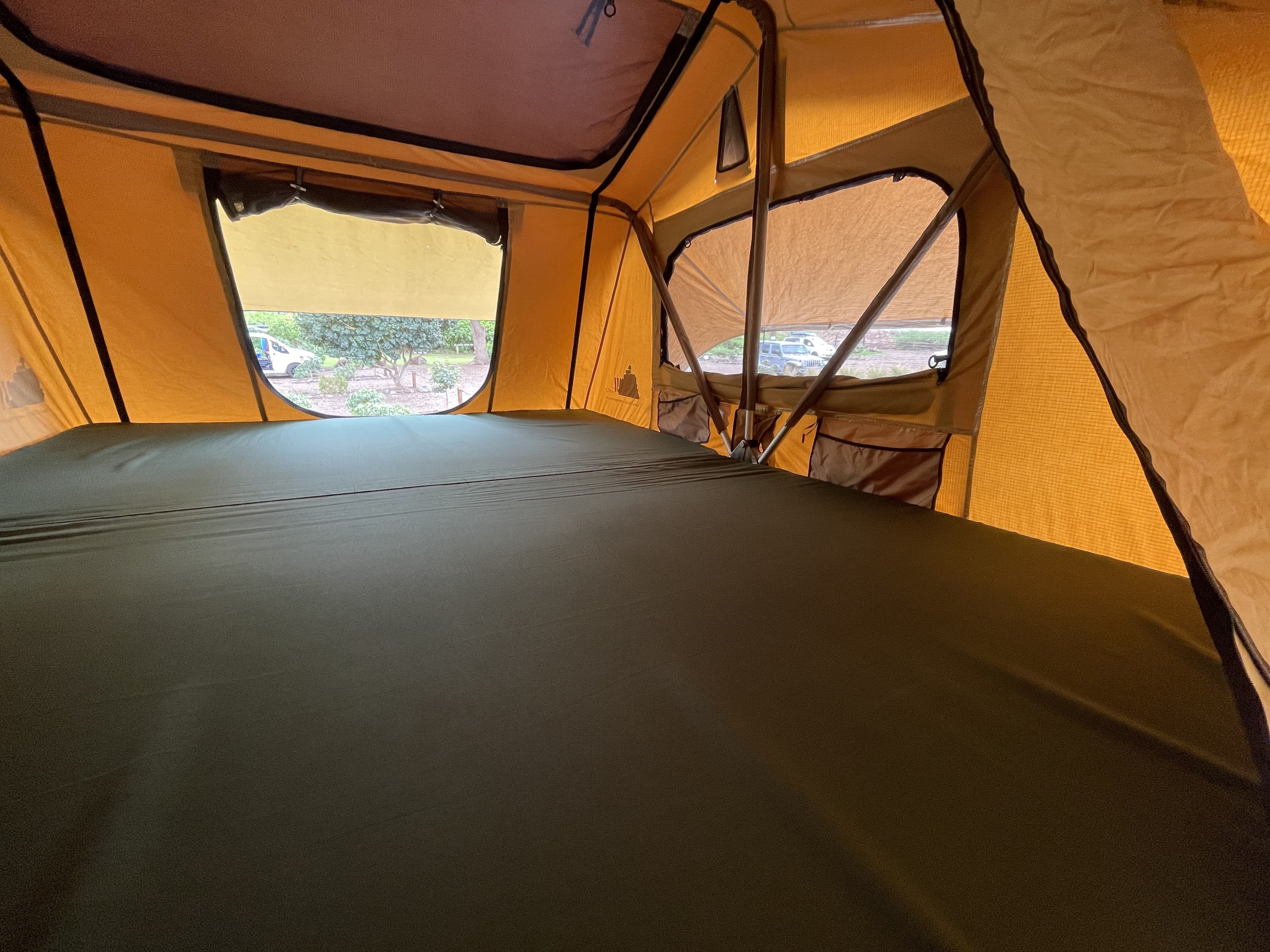 Comfortable sleeping space inside an RV rental rooftop tent, featuring a large green mattress and clear outdoor views.. Jeep Wrangler 2017