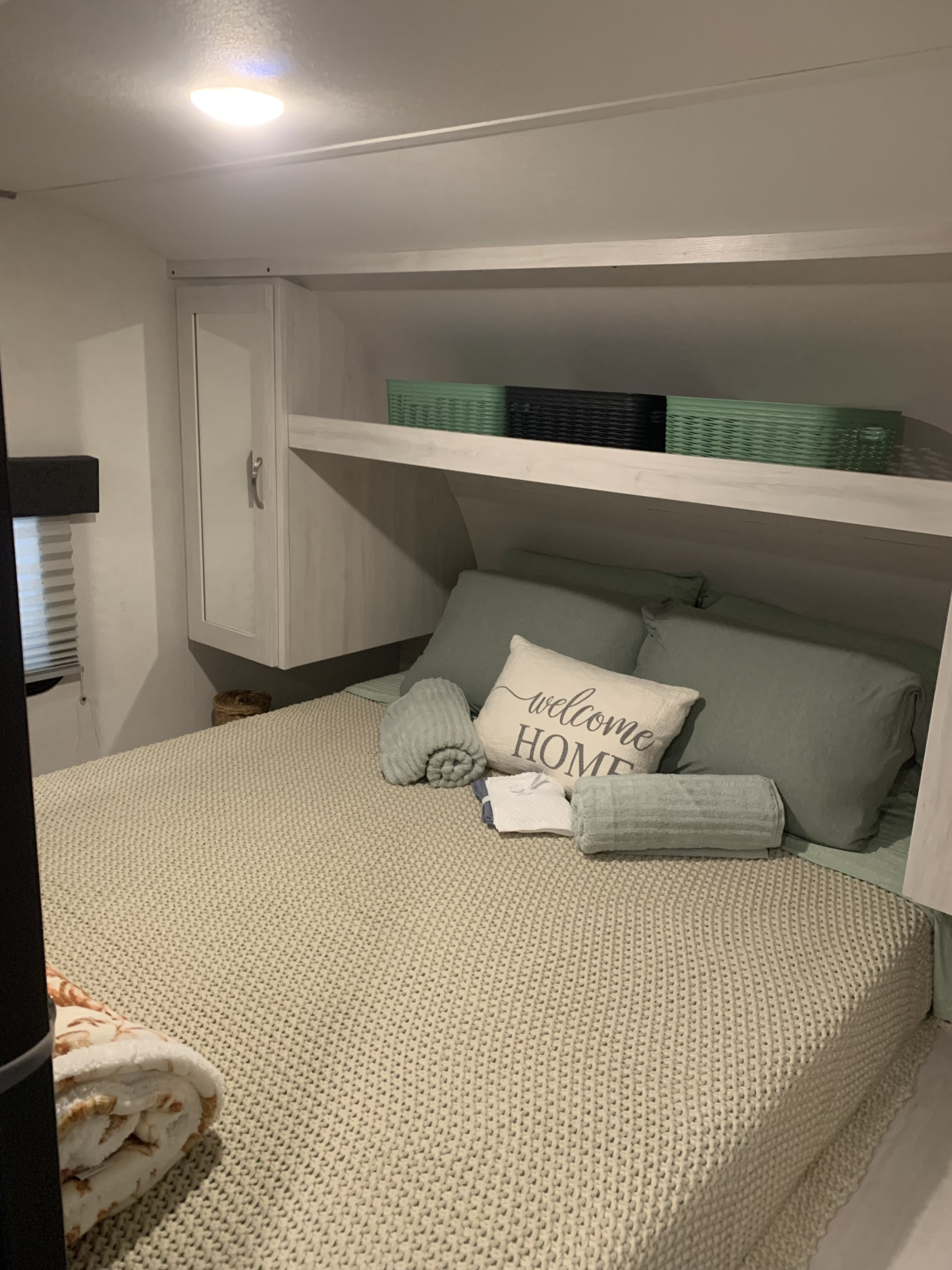 Inside an RV rental, a welcoming bedroom with soft green bedding, textured blanket, and overhead storage.. Prime Time Tracer 2022