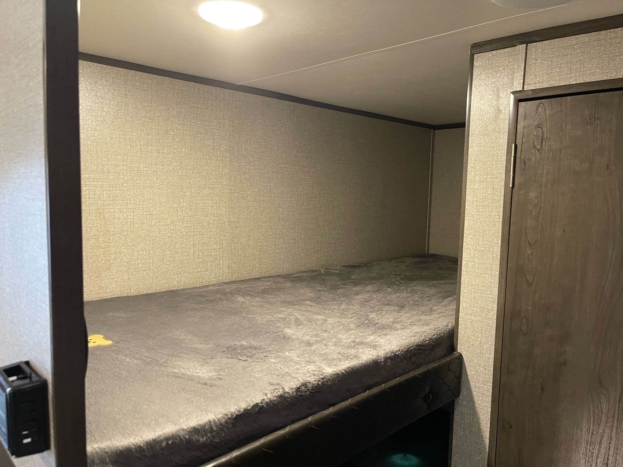 RV rental interior shows a cozy bunk bed with gray fuzzy blanket, textured walls, and overhead light.. Jayco Jay Flight SLX 2021