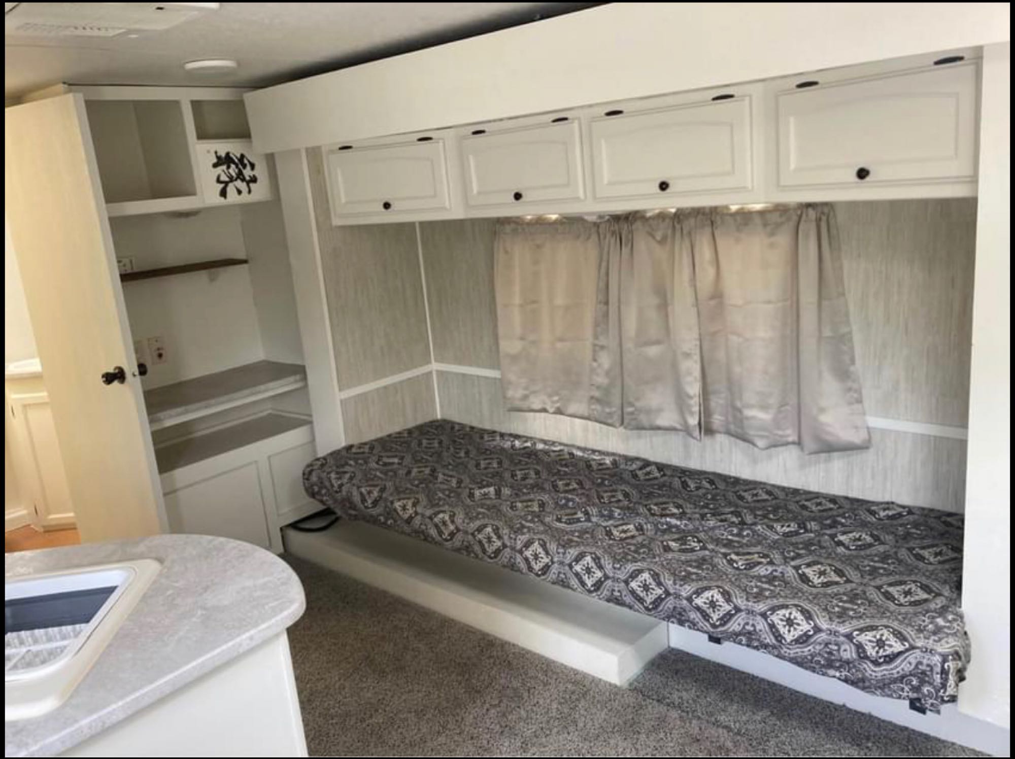 Inside this rv rental: a cozy single bed, overhead storage cabinets, shelves, and a kitchen counter. Perfect for travel.. Heartland North Trail 2009