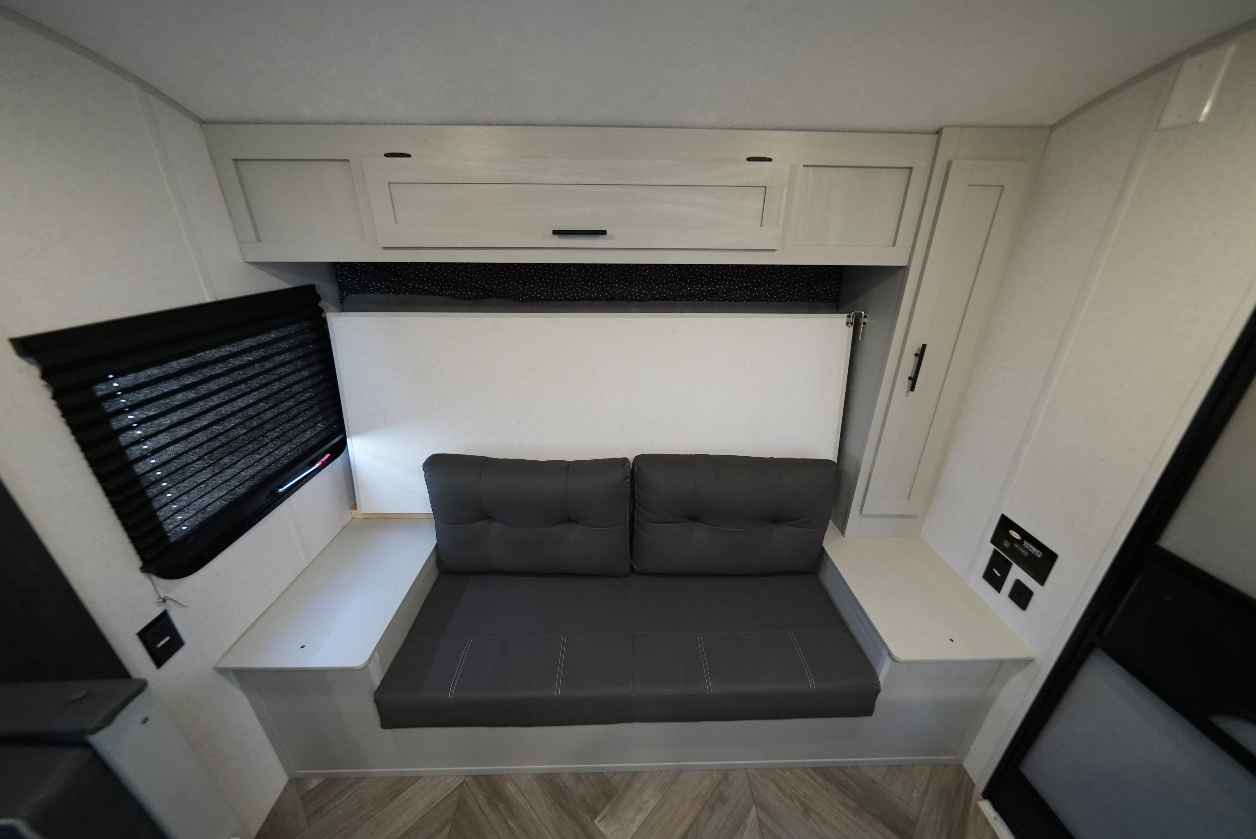 RV rental interior featuring a gray sofa, overhead cabinets, and a fold-down bed/table. Compact and functional space.. Wildwood FSX 178BHsk 2022