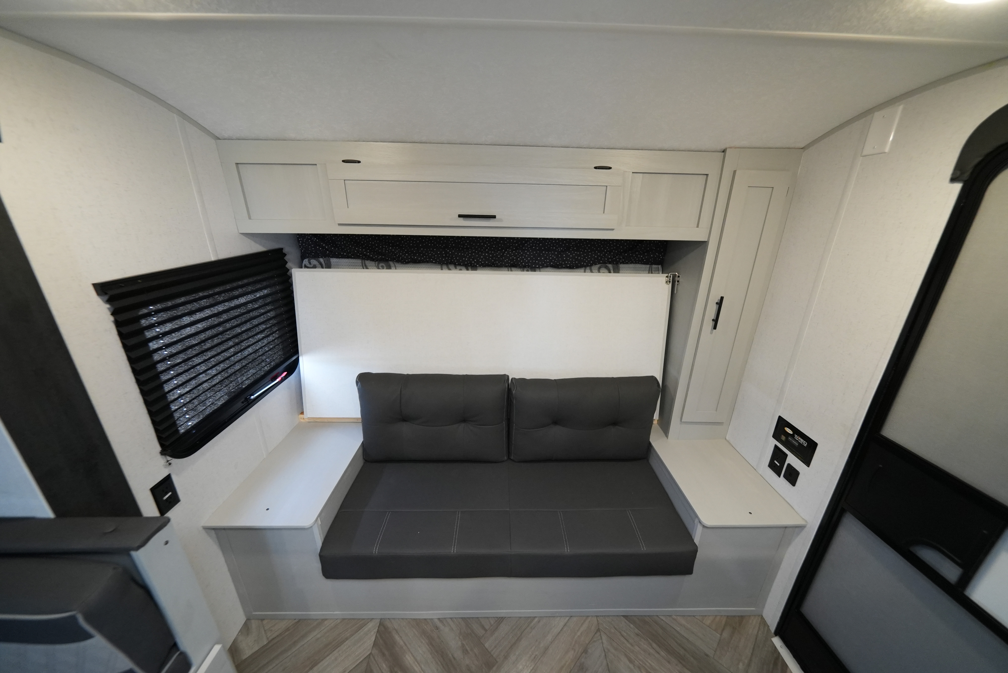 Compact RV rental interior featuring a gray convertible sofa/bed, white overhead cabinets, and window.. Wildwood FSX 178BHSK 2022