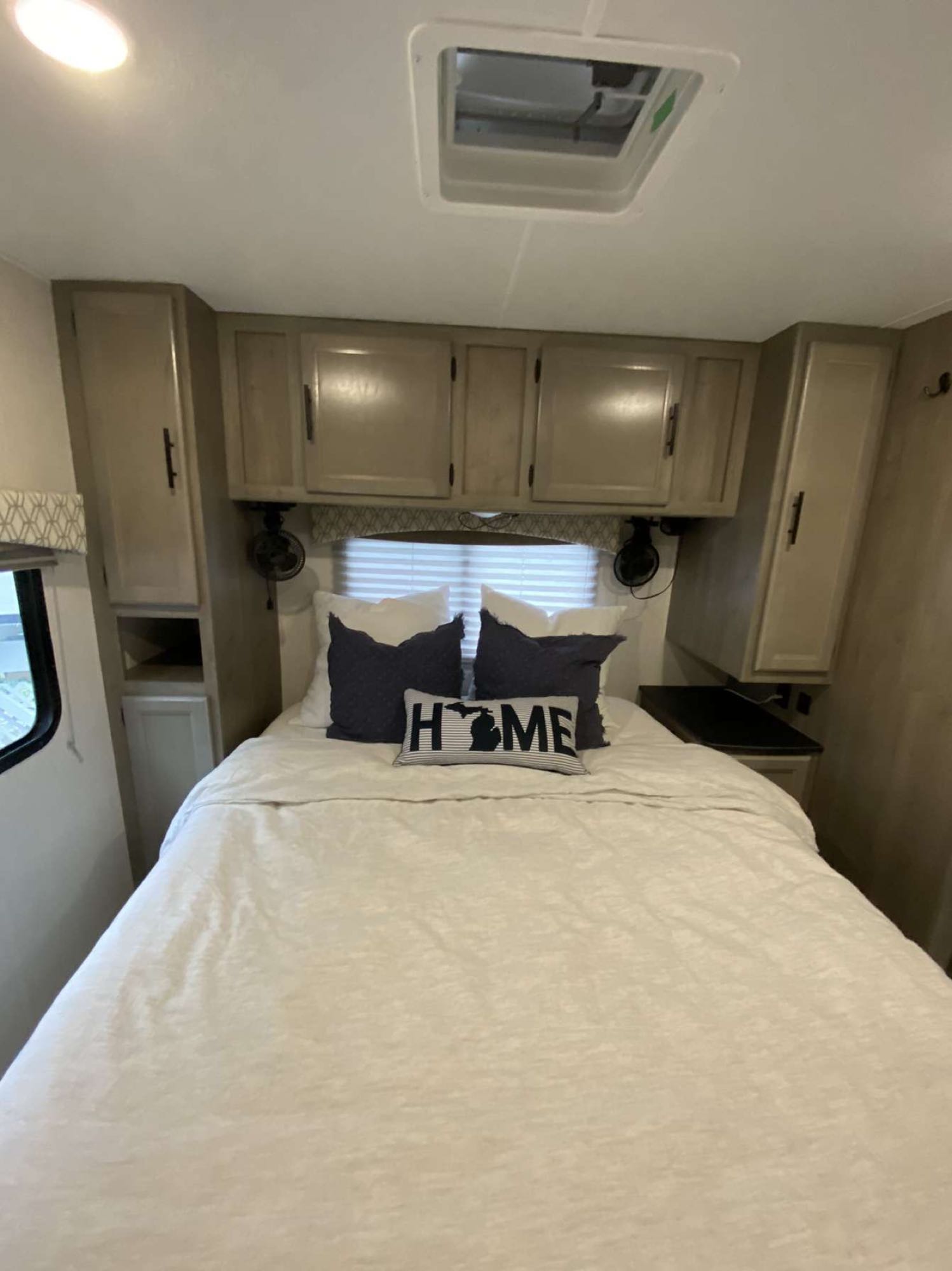 Cozy RV rental bedroom featuring a comfortable bed with white linens, overhead cabinets, and a window with blinds.. Coachmen Freelander 2021