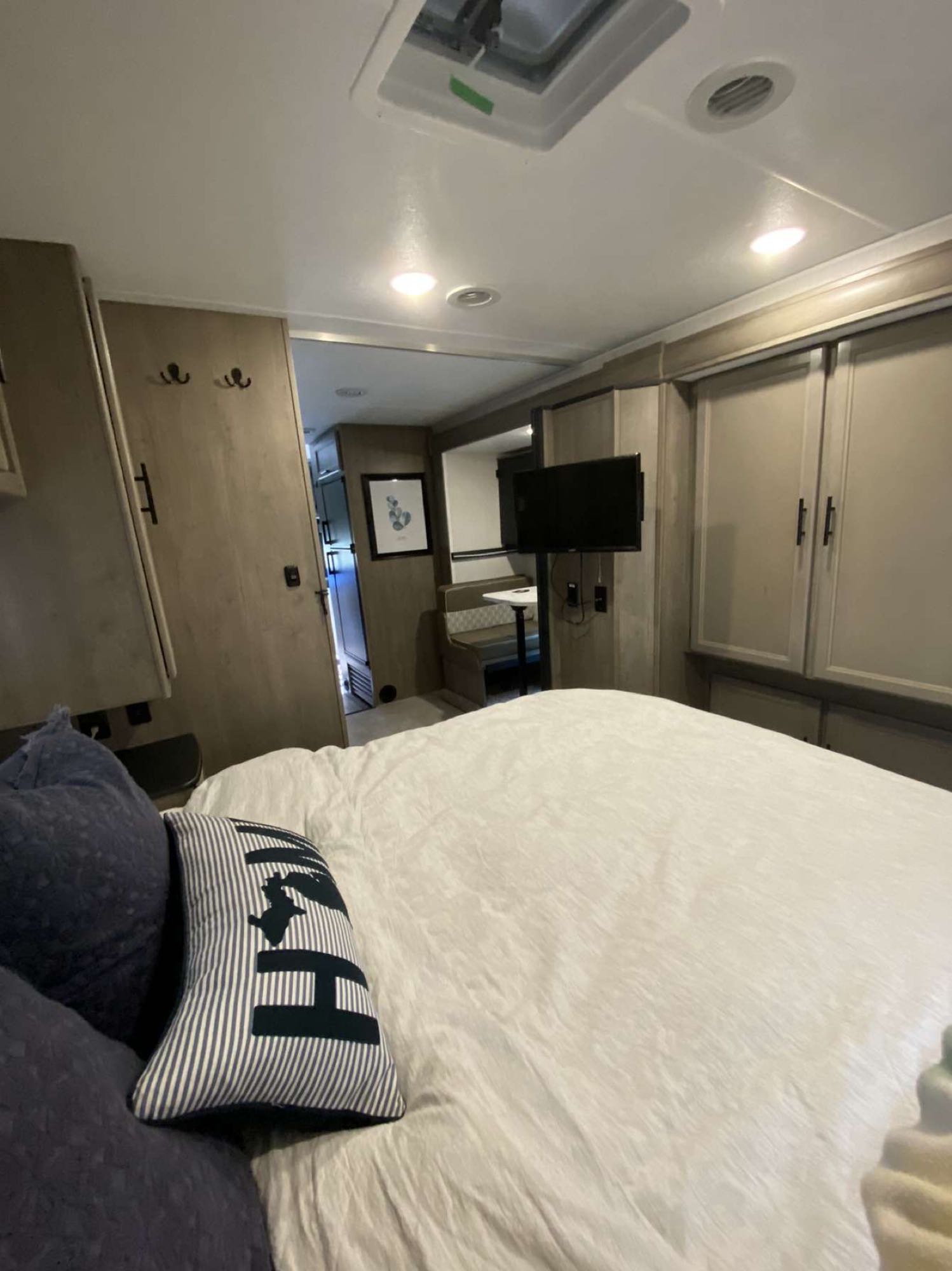 Modern RV rental interior, a cozy bedroom looking into the living area with a mounted TV and dining booth.. Coachmen Freelander 2021