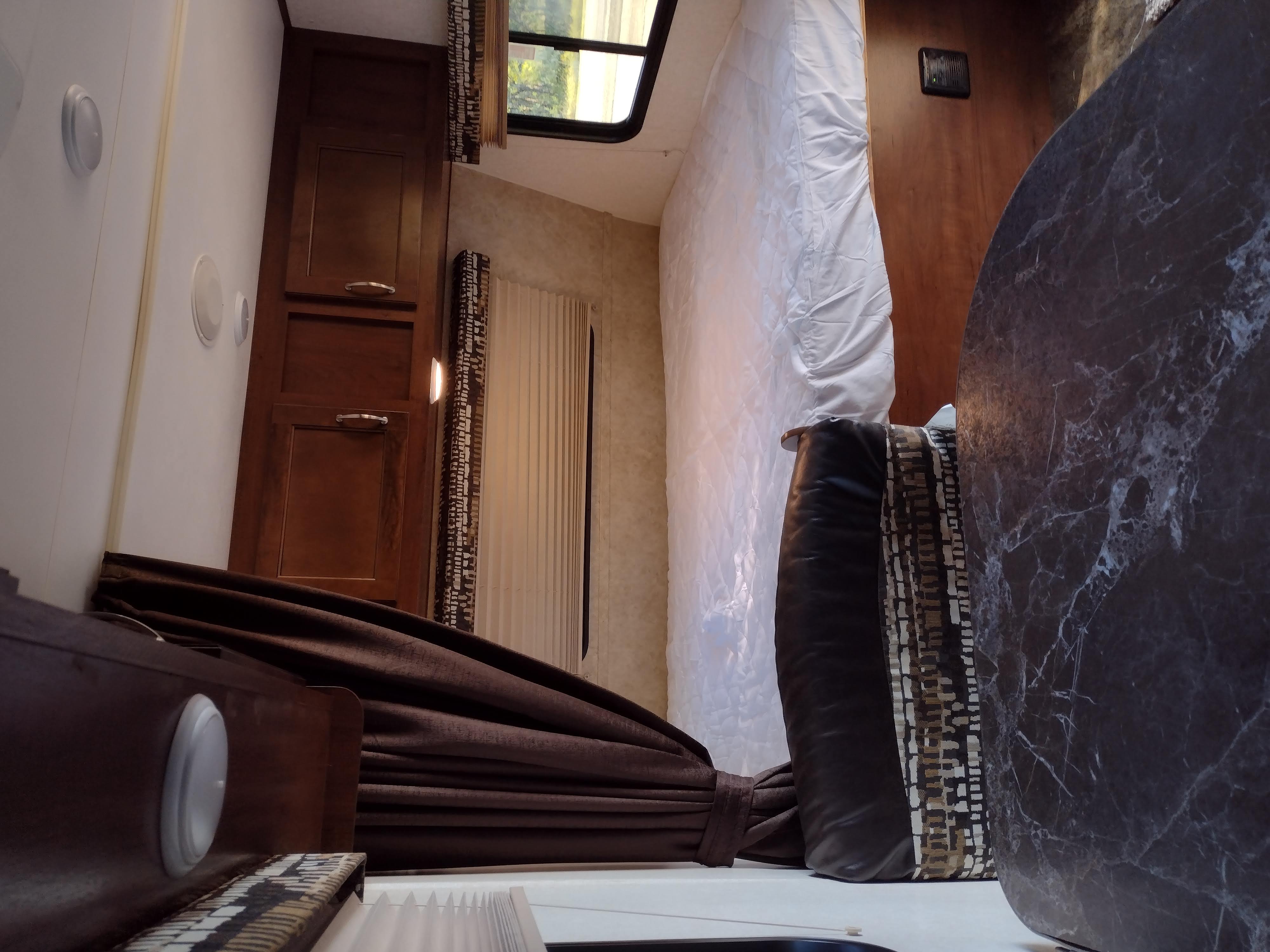Cozy RV rental interior, featuring a compact living space with a bed, patterned curtains, and a marbled table.. Jayco Jay Flight 2017
