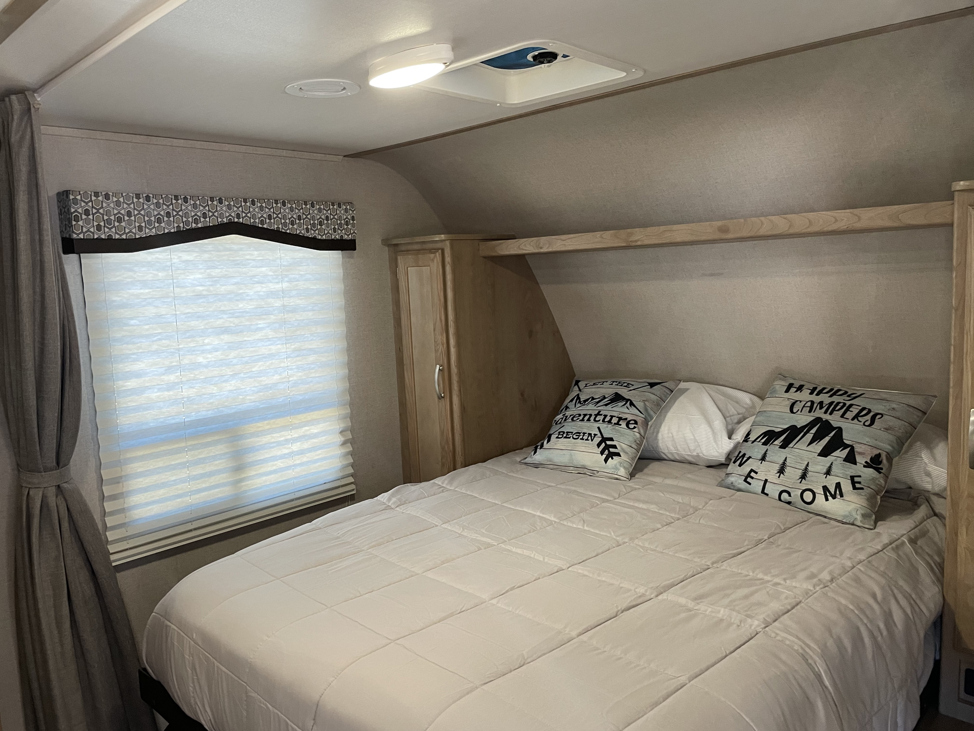 Cozy RV rental bedroom features a comfy bed with decorative pillows, window, and built-in storage.. Winnebago Micro Minnie 2020