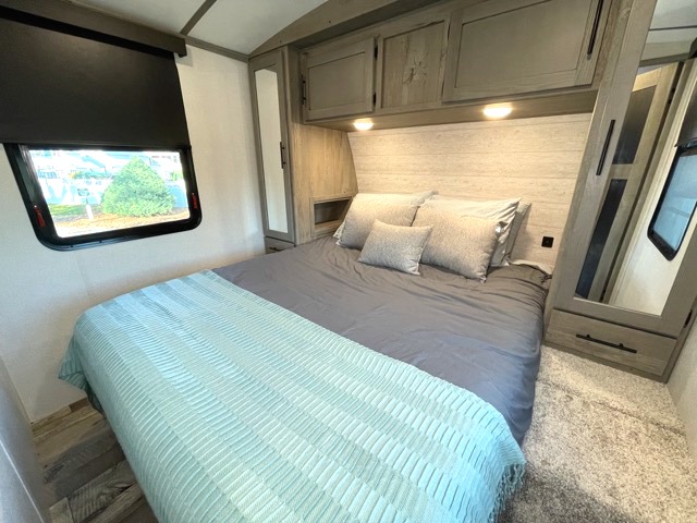 Experience comfort in this RV rental's bedroom, featuring a queen bed with soft bedding, built-in storage, and window.. Keystone RV Outback 2021