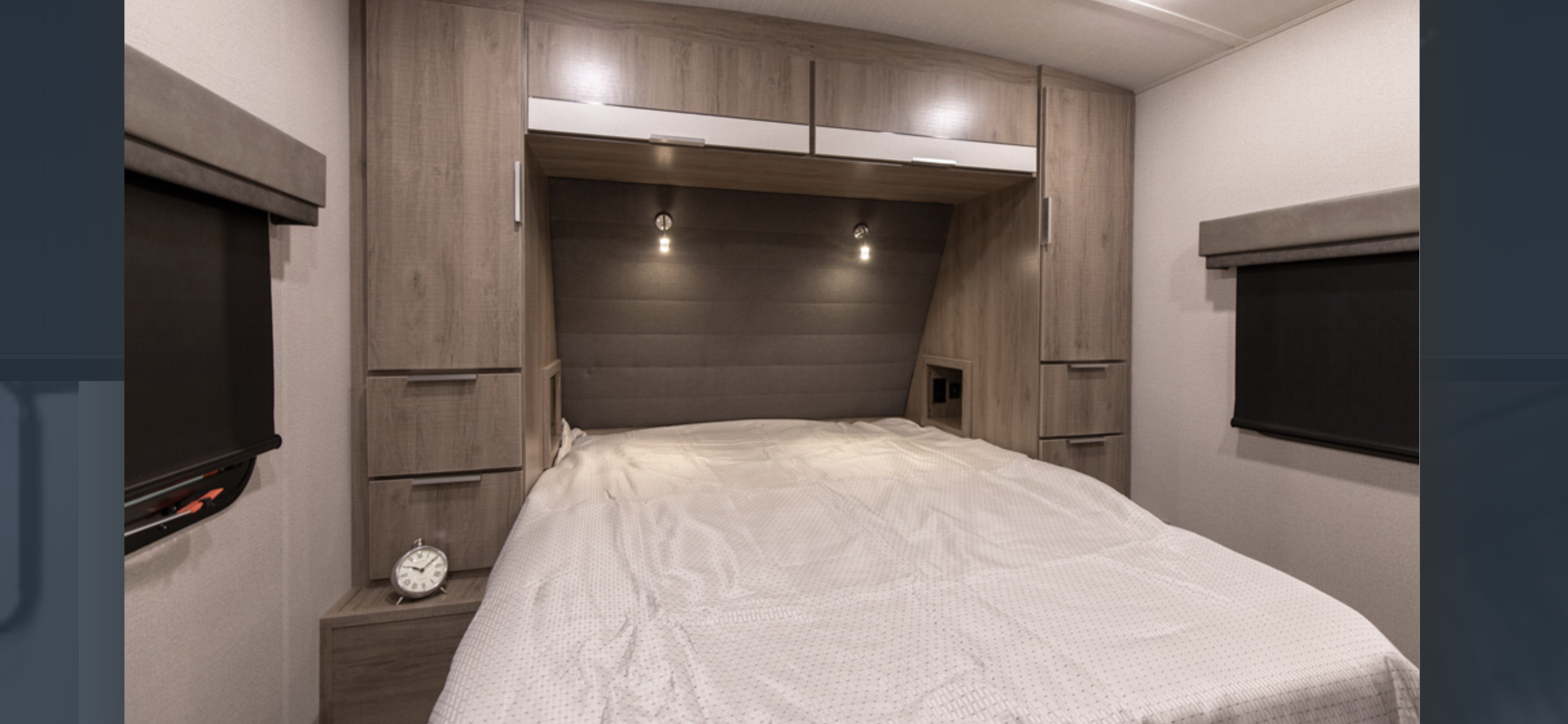 This RV rental bedroom features a cozy bed, built-in cabinets, and warm bedside lighting. Perfect for travelers.. Grand Design Imagine 2021