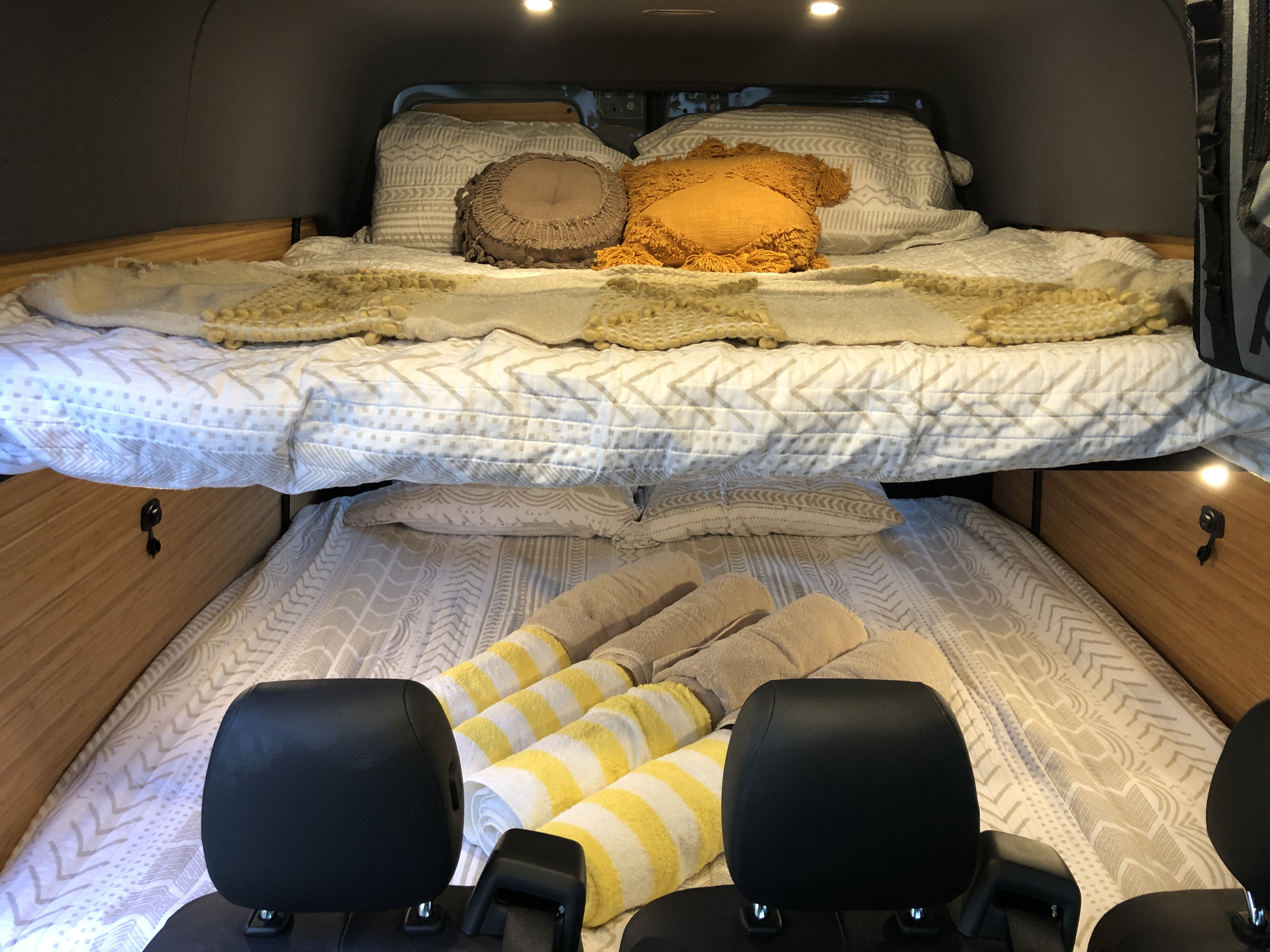 Cozy rv rental interior featuring bunk beds with patterned bedding and decorative pillows. Rolled towels await on the lower bed.. Mercedes-Benz Sprinter 2021