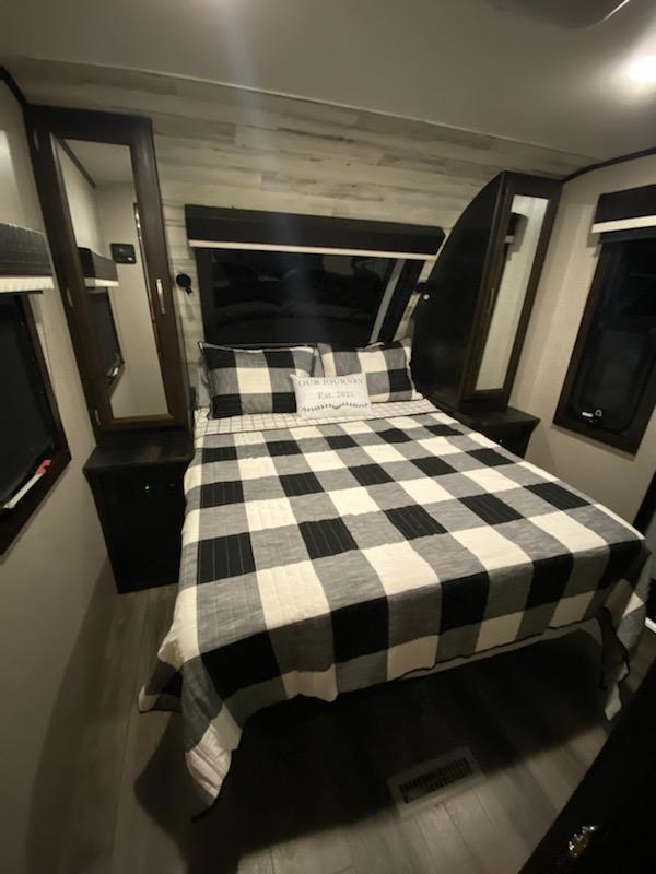 Cozy RV rental bedroom with a queen bed, buffalo check bedding, nightstands, and storage. Ideal for comfortable travel.. Jayco White Hawk 29BH 2021