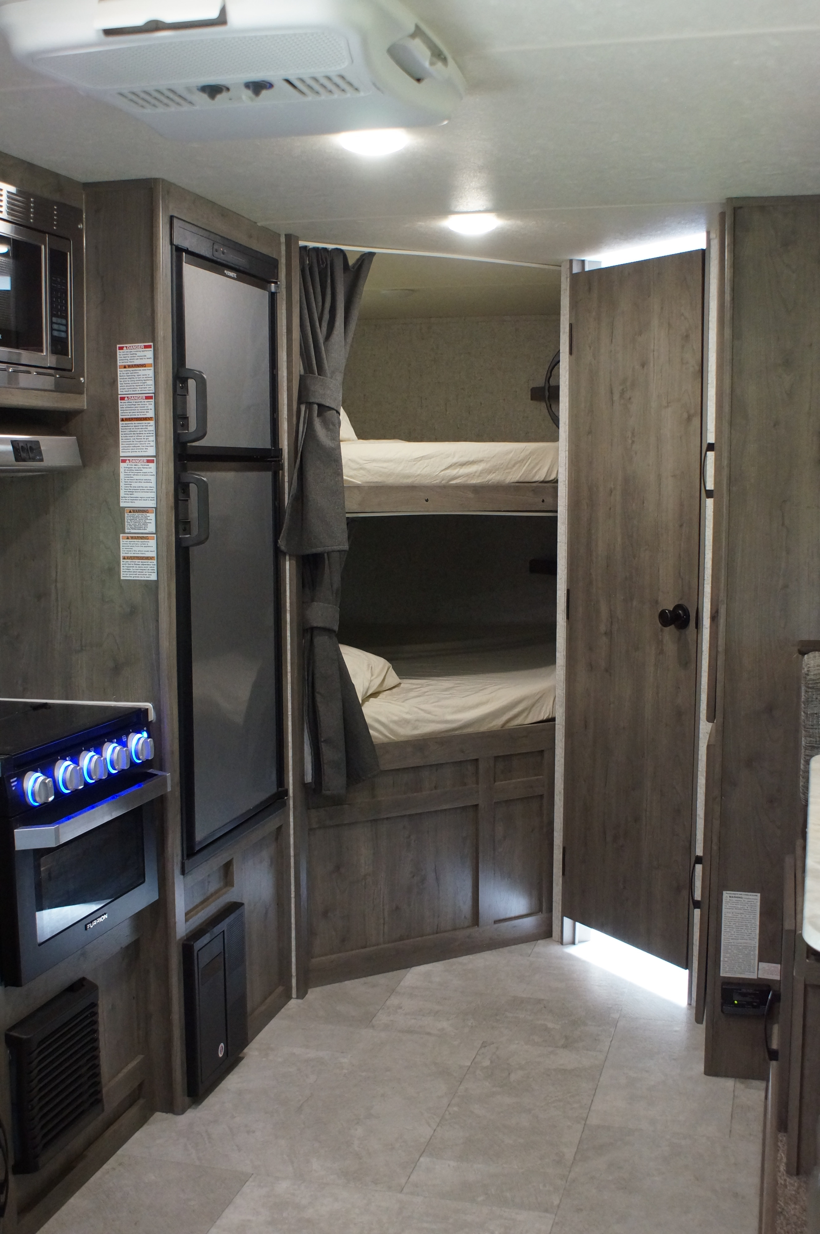 RV rental interior. Kitchenette with microwave, fridge, and stove. Bunk bed area visible with curtains. Tiled floor and ceiling AC unit.. Apex Nano 245 BHS 2020