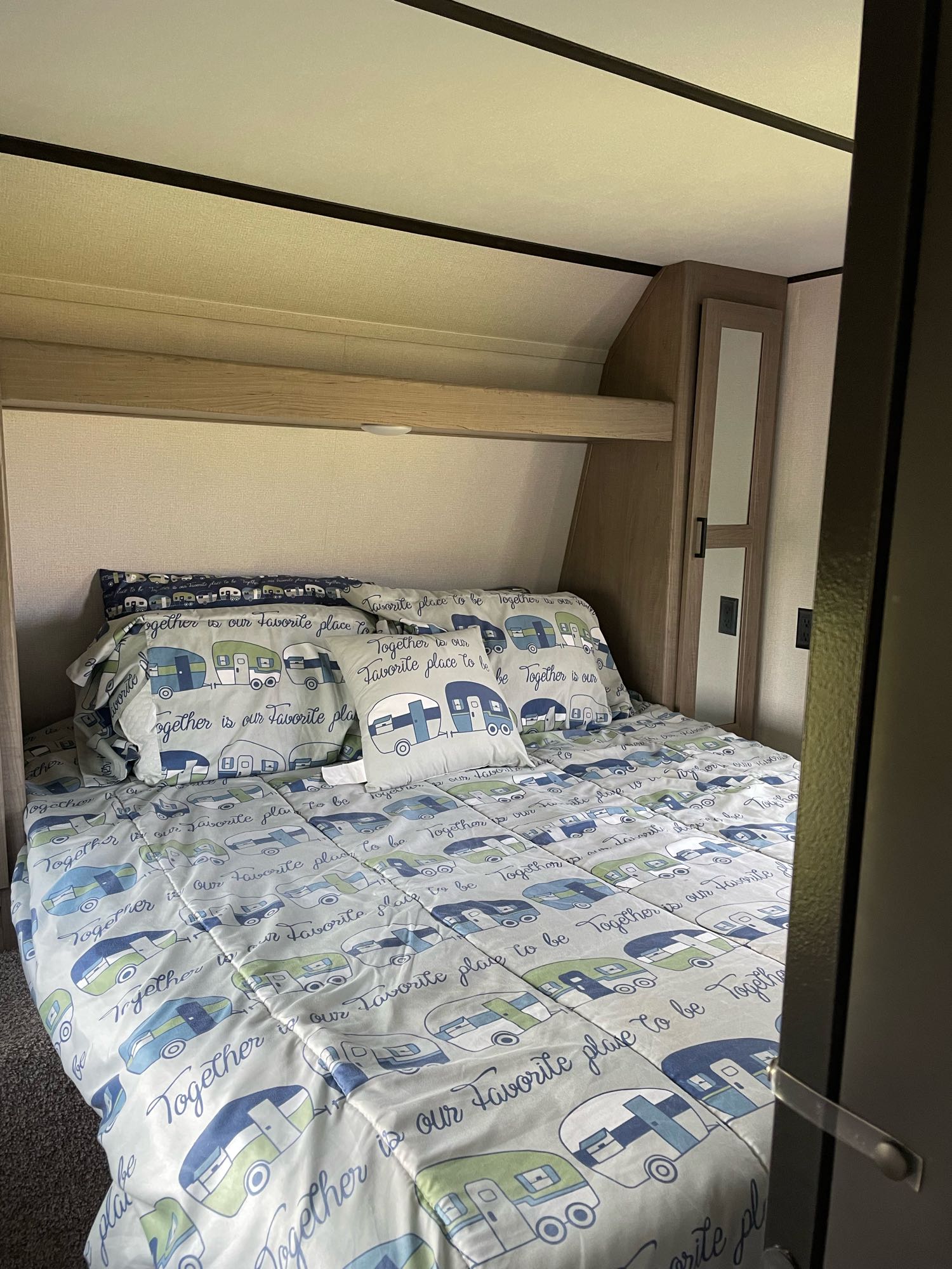 This RV rental bedroom features a cozy bed with camper-themed bedding, an overhead shelf, and a mirror, perfect for travel.. Keystone Hideout 2021