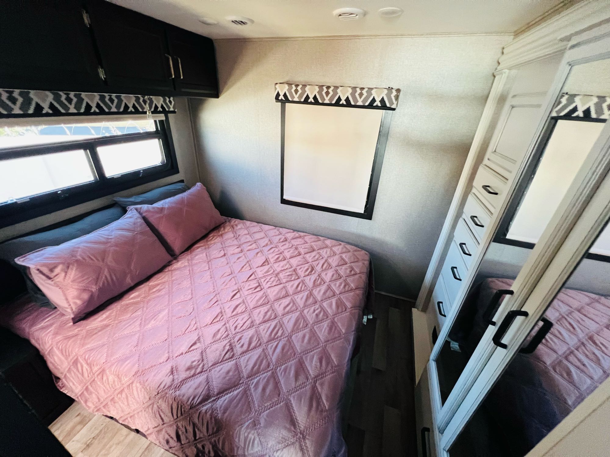 RV rental bedroom: pink quilted bed, overhead cabinets, and a mirrored wardrobe for a comfortable stay.. Jayco Alante 2021