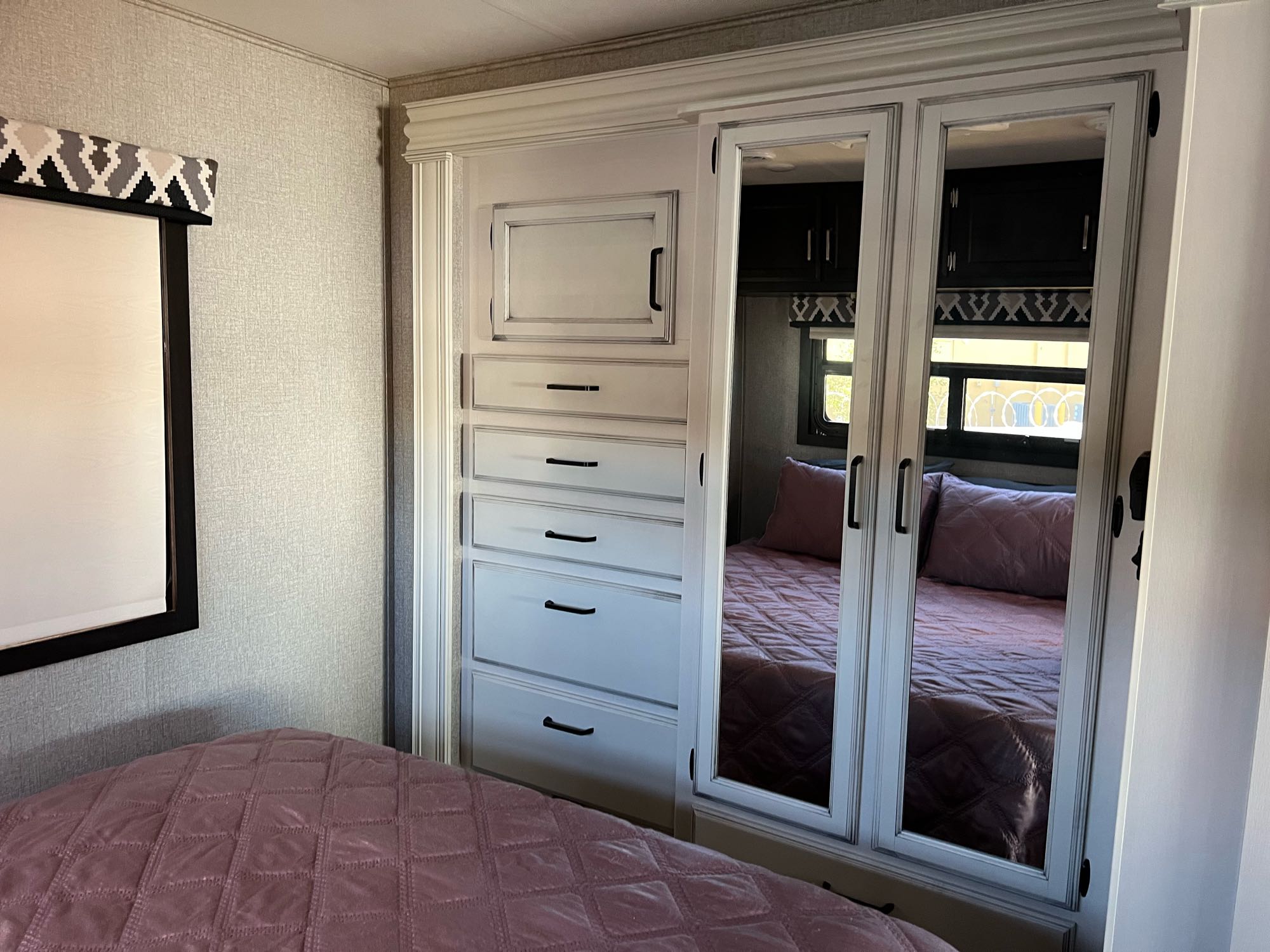 Compact RV bedroom featuring built-in storage with mirrored doors, a comfortable bed, and stylish valance. Perfect for your next RV rental adventure.. Jayco Alante 2021