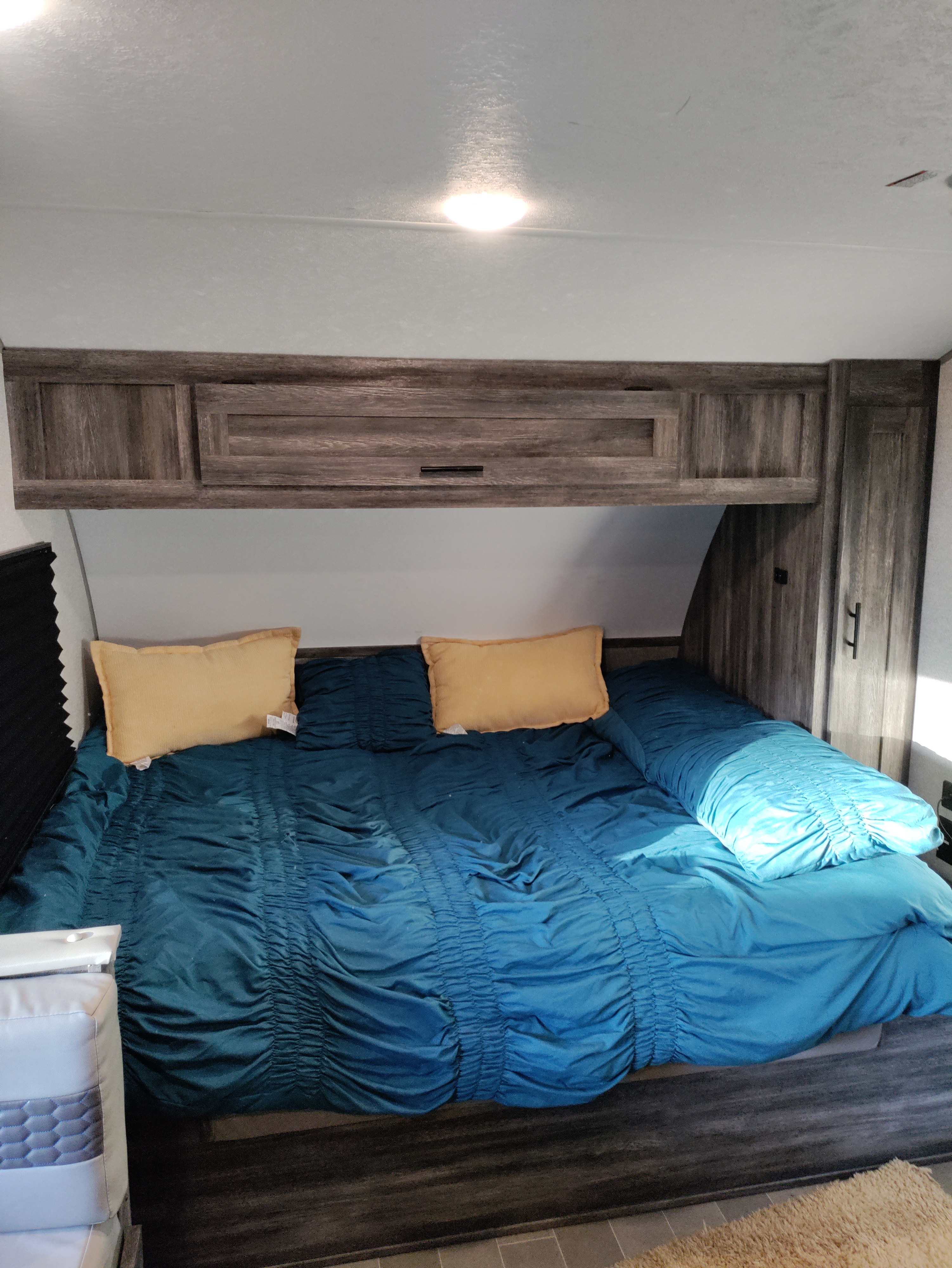 Cozy RV rental bedroom features a blue comforter, yellow pillows, and dark wood-look storage cabinets.. Forest River Salem FSX PLATINUM 2020