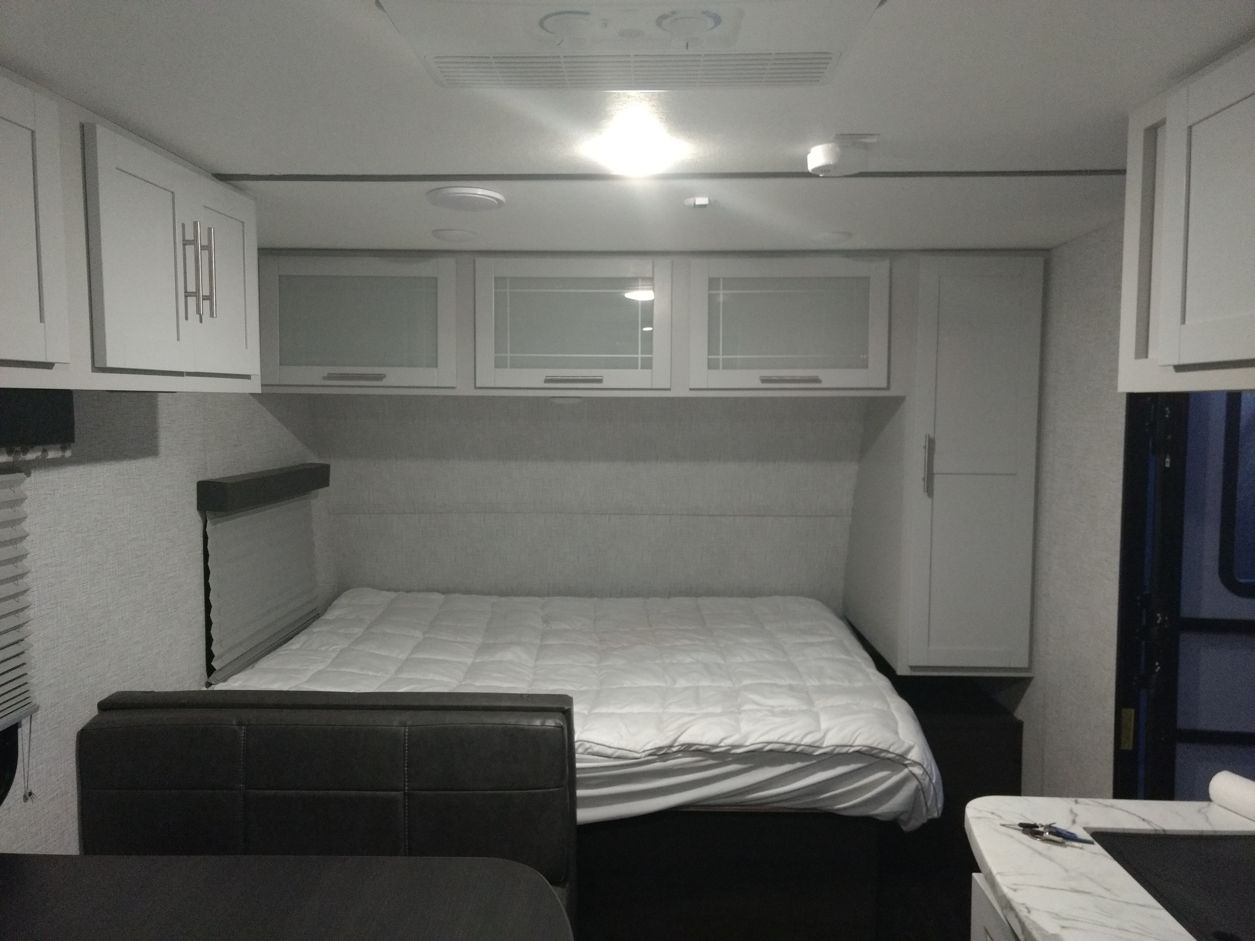 Inside an RV rental: a cozy bedroom with a white queen bed, bright overhead cabinets, and built-in storage.. Keystone RV Bullet Crossfire 2021