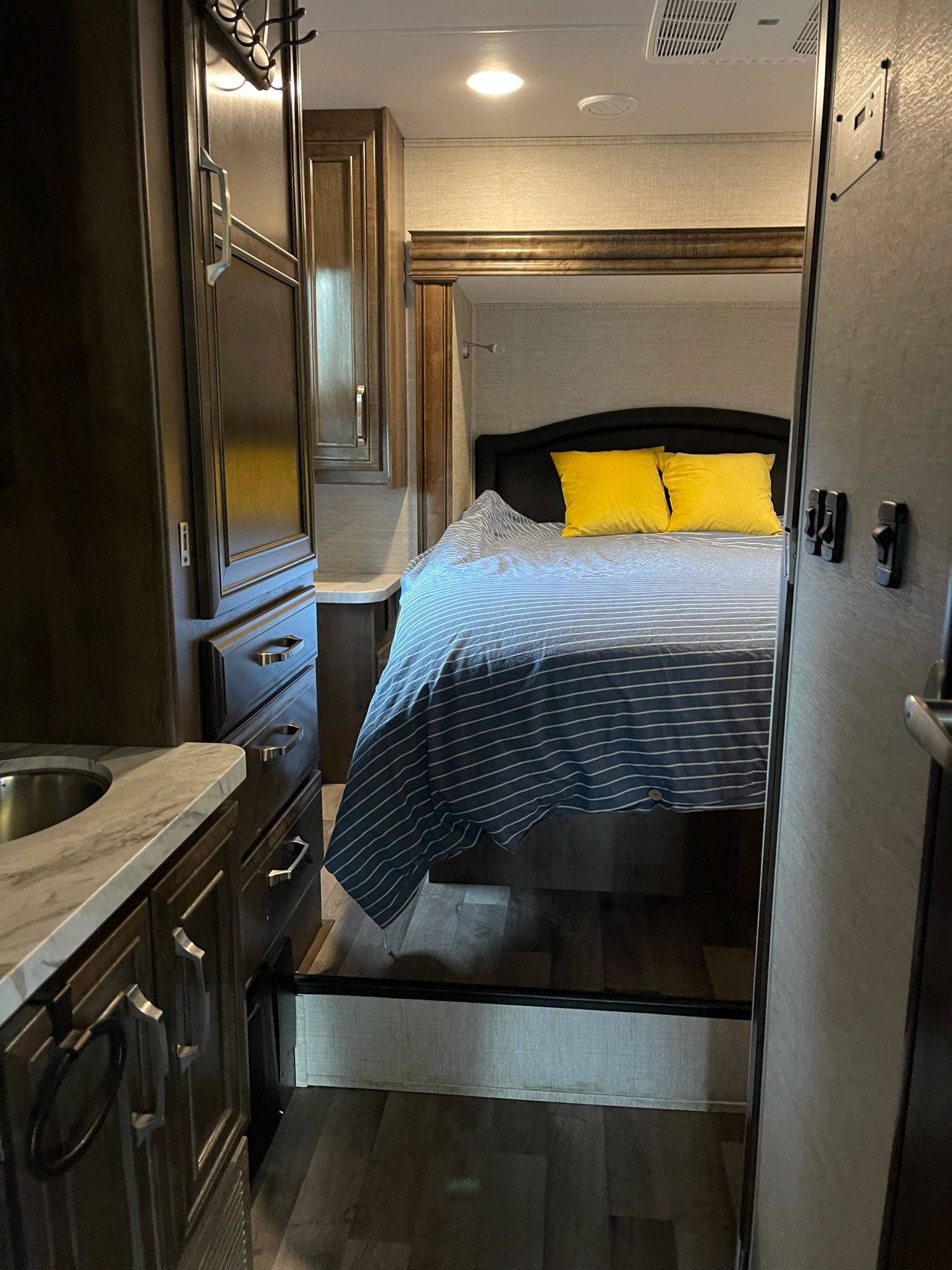 Experience this RV rental's cozy bedroom. It features a bed with striped covers, yellow pillows, and dark wood cabinets and sink.. Jayco Greyhawk 2021