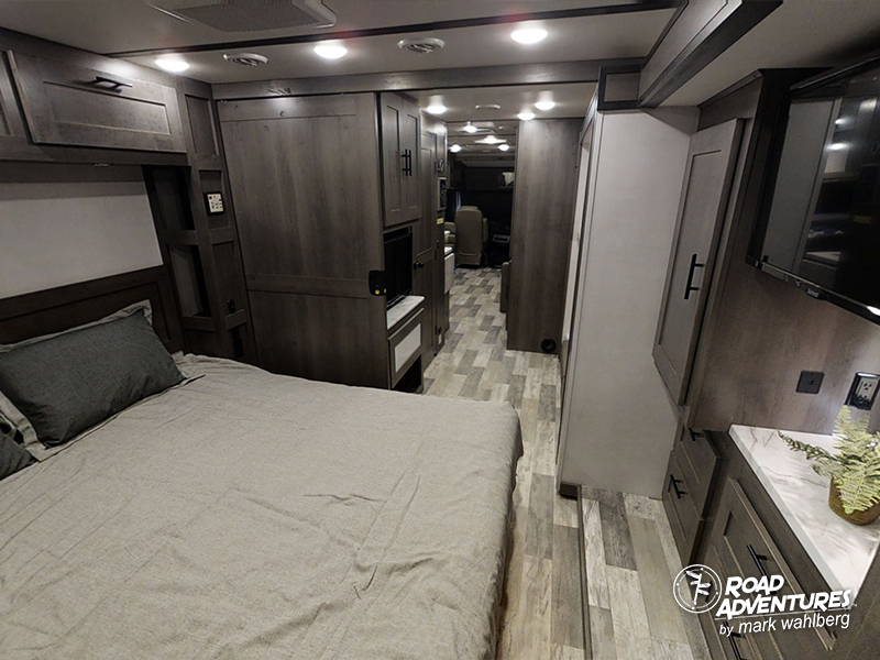 Step inside this RV rental: a cozy bedroom on the left, with modern wood cabinetry, storage, and TV along a central aisle.. Forest River Fr3 2021