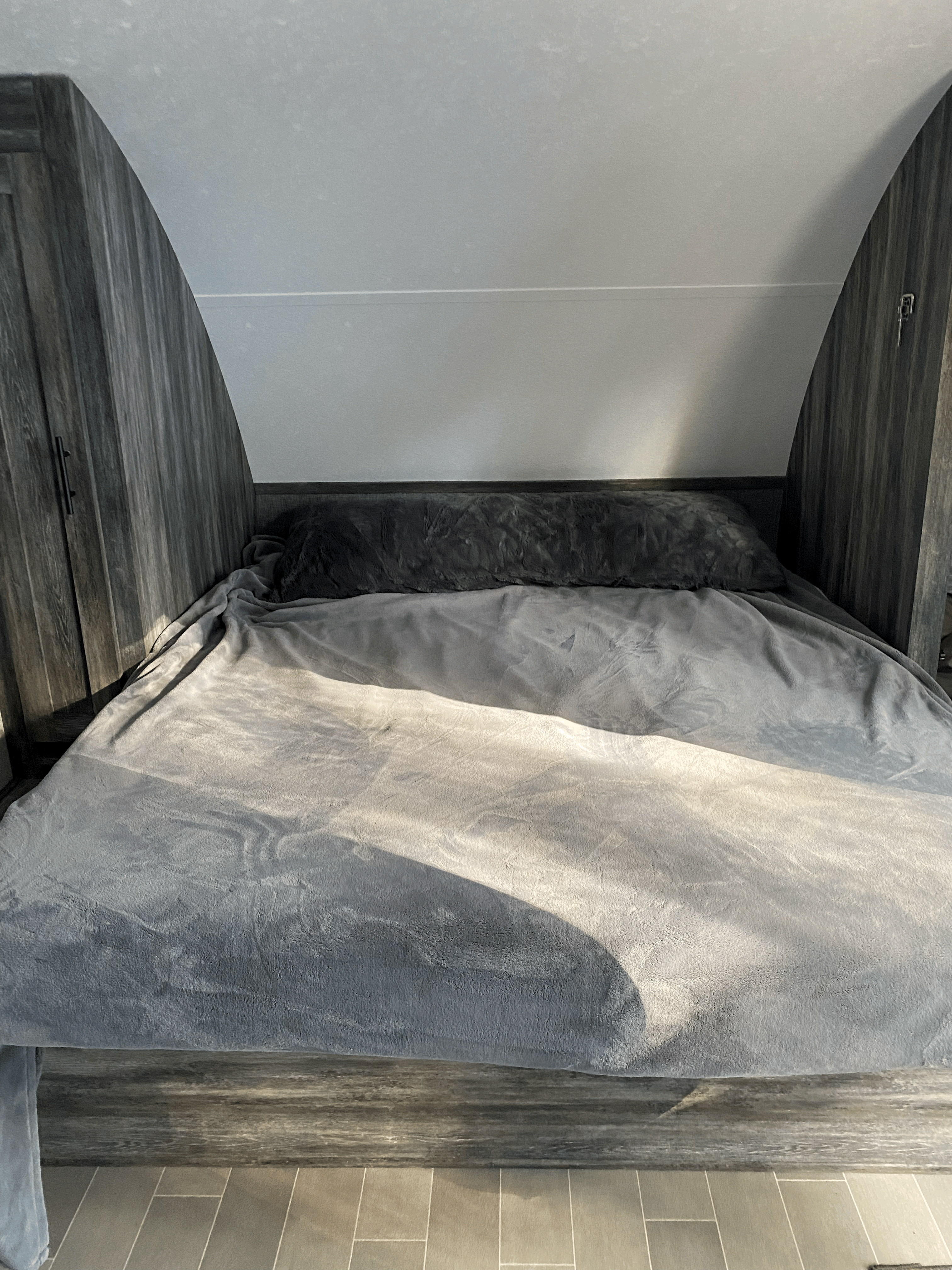 Cozy RV rental bedroom featuring a grey bed, dark wood-paneled walls, and sunlight streaming across the blankets.. Forest River Salem FSX 2021