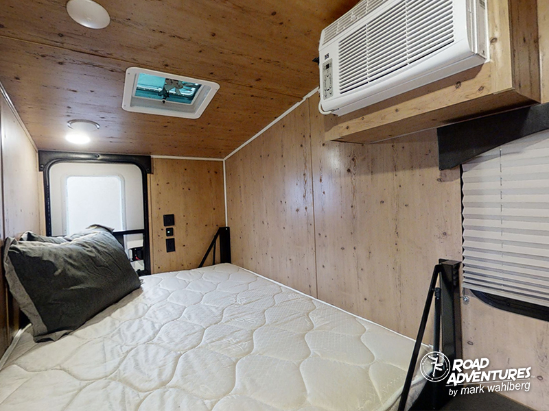 This RV rental interior offers a cozy bedroom space with a bed, wood walls, AC, and roof vent for comfortable travel.. Sunset Park Sunray 2021