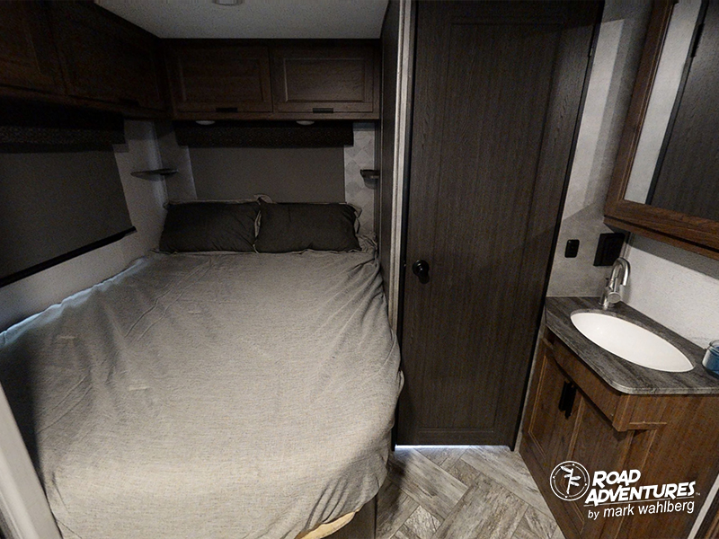 Queen bed, compact vanity, and overhead storage cabinets in a modern RV rental. Ready for your travel adventures.. Forest River Sunseeker 2022