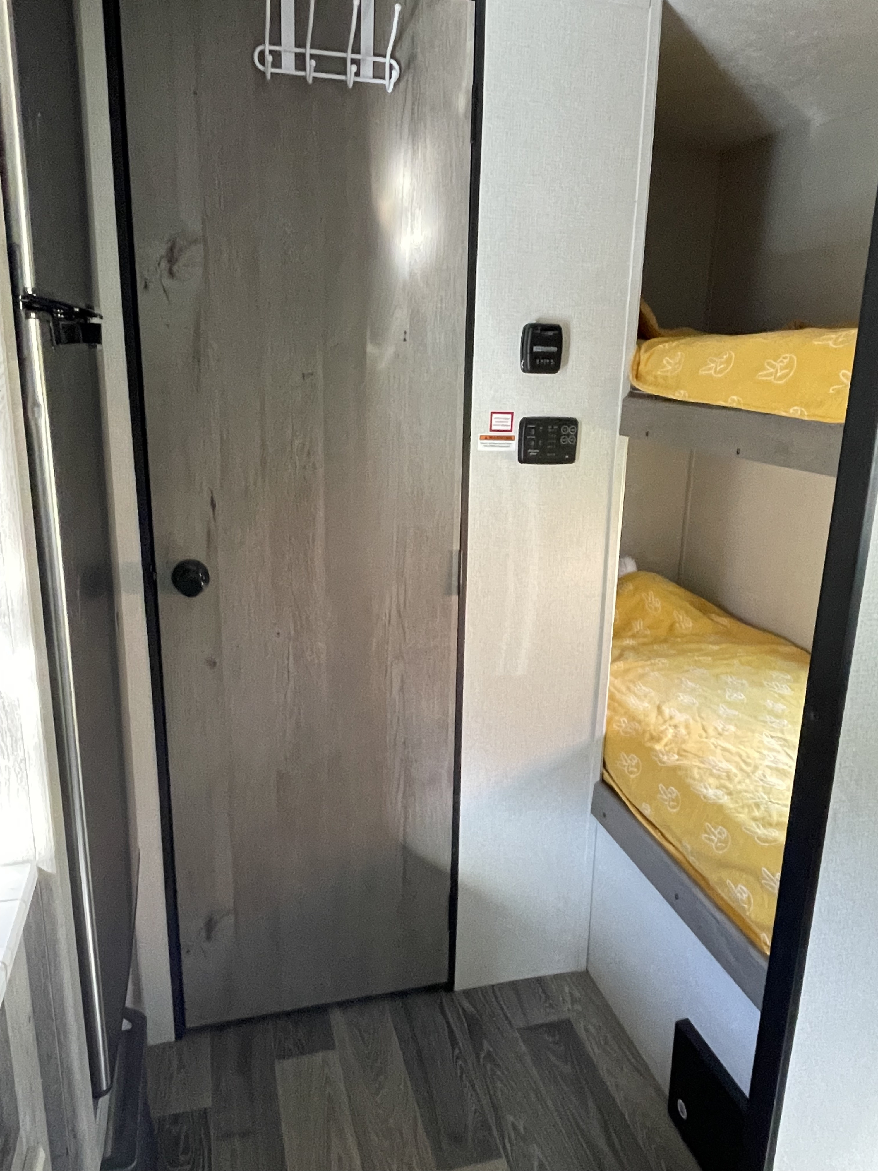 This RV rental interior features compact bunk beds with yellow peace sign bedding, a wood-look floor, door, and wall-mounted controls.. Keystone RV Springdale 2021
