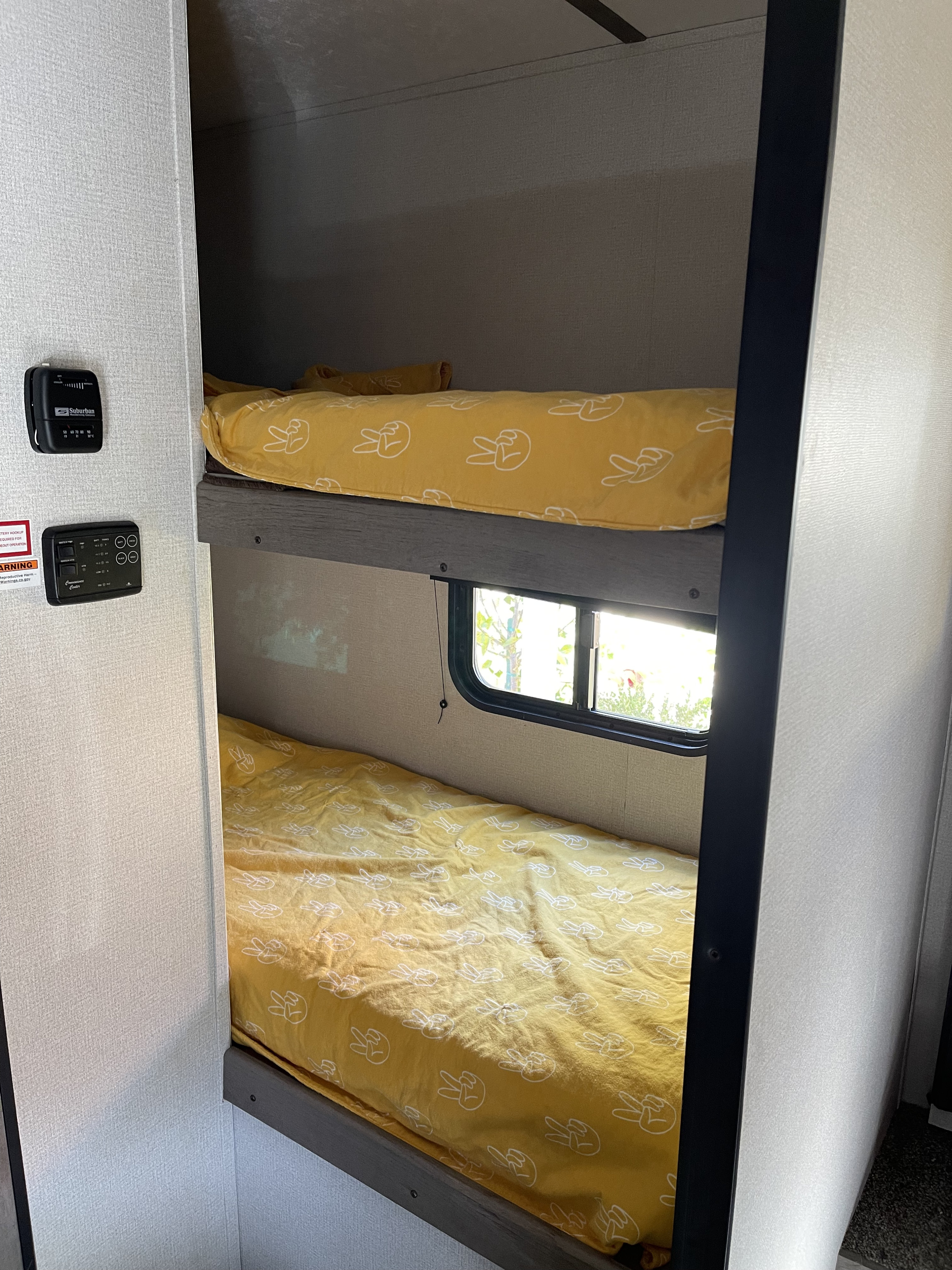 Bright yellow peace-sign bedding on bunk beds in an RV rental, with a window and control panels visible on the wall.. Keystone RV Springdale 2021