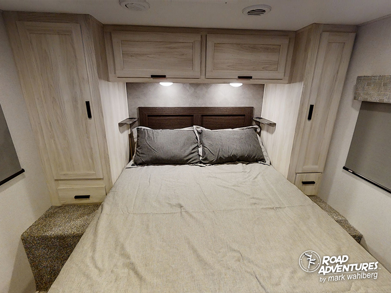 This inviting RV rental bedroom features a comfy bed, light wood overhead cabinets, and tall side wardrobes for travel.. Forest River Sunseeker 2022