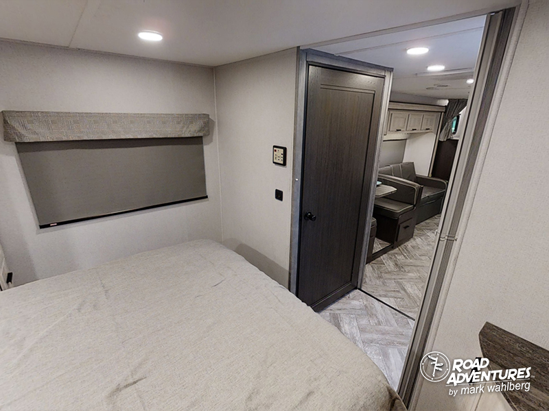 Modern RV rental interior: bedroom with bed & window, connecting to a compact living area with a sofa.. Forest River Sunseeker 2022