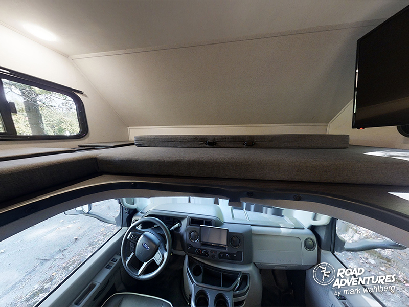 Experience RV rental comfort: the driver's cockpit below a cozy overhead bunk with a view window and TV.. Forest River Sunseeker 2022