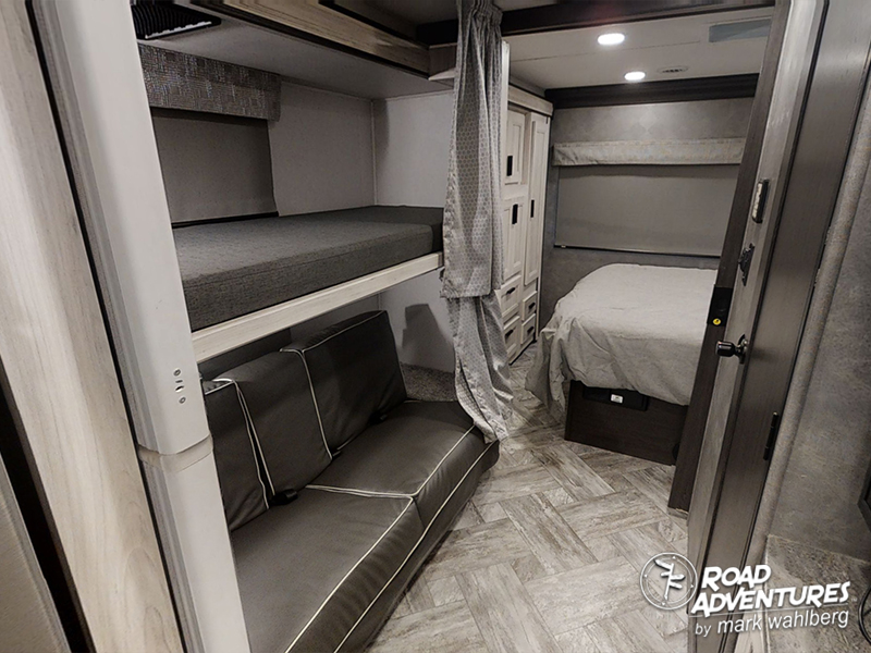Interior of an RV rental showing bunk beds, a lower sofa, and a separate bedroom with a bed and wardrobe.. Forest River Sunseeker 2022