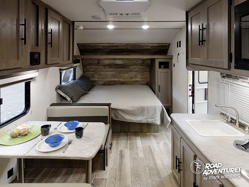 RV rental interior features a cozy bed area, dinette, and kitchen space with overhead cabinets.. Gulf Stream Amerilite 2021