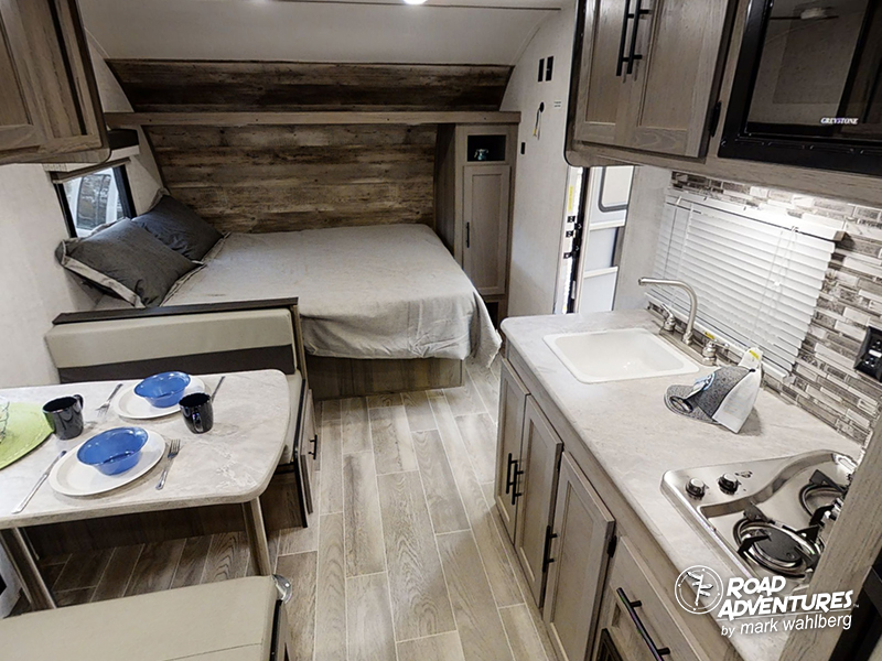 This RV rental interior features a cozy bed, dining area, and compact kitchen. Perfect for travel adventures!. Gulf Stream Amerilite 2021