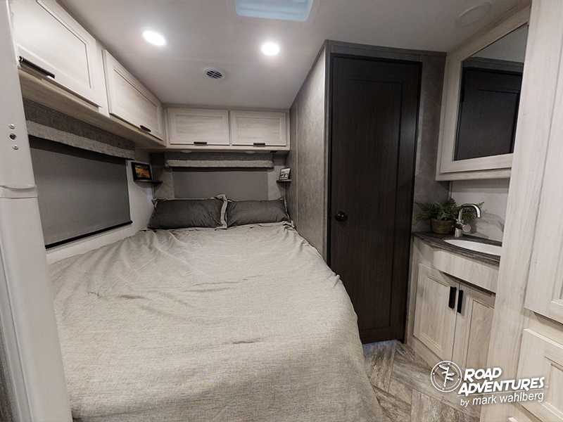 Spacious RV rental bedroom featuring a large bed, overhead storage, and a convenient compact bathroom area with sink and mirror.. Forest River Sunseeker 2022