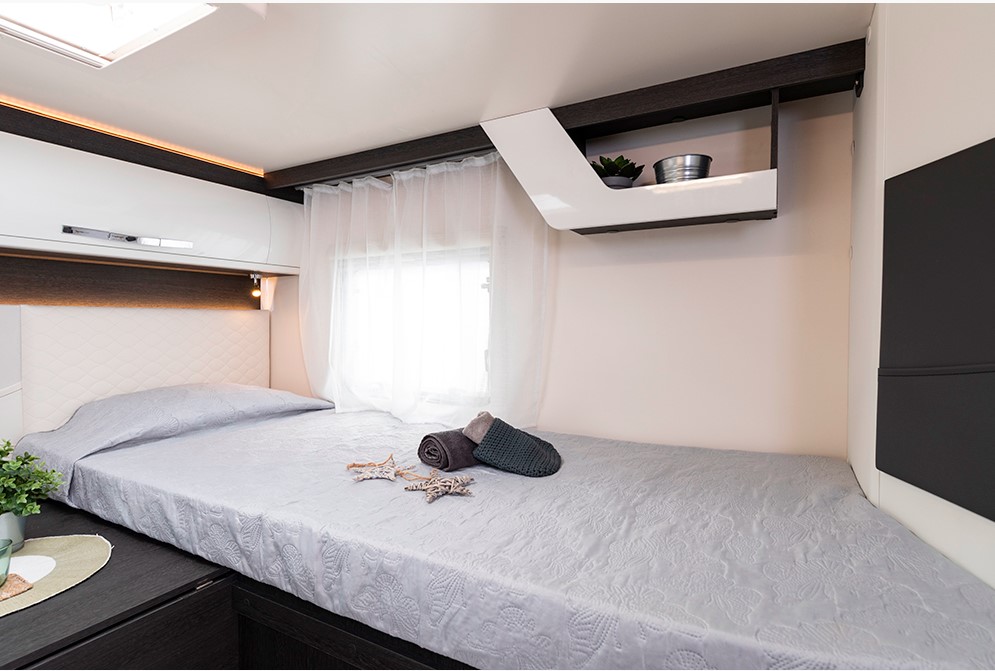 Modern rv rental bedroom showing a light grey bed, overhead cabinets, & sheer curtains. Relaxing travel space.. Roller Team Zefiro 685 2026