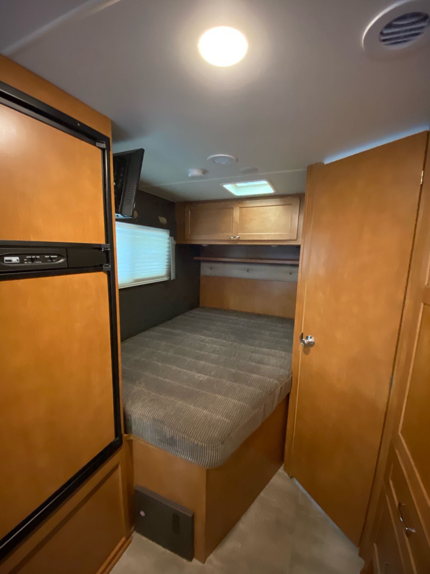 This rv rental offers a compact bedroom with a striped bed, refrigerator, wood cabinets, and a door on the right.. Winnebago Minnie Winnie 2018