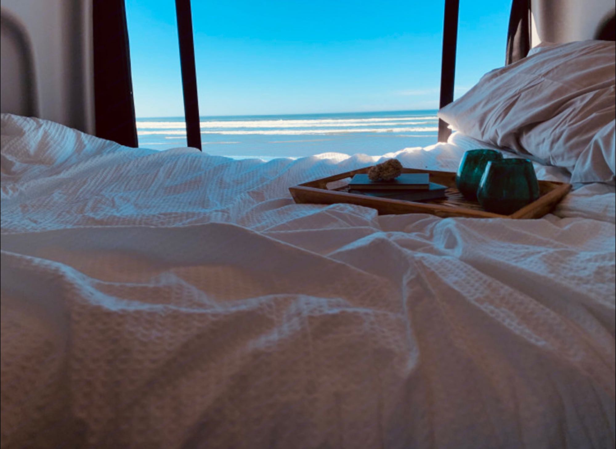 Wake up to ocean views! Comfy bed, tray with drinks & book in this cozy RV rental. Perfect escape.. Winnebago Revel 2022