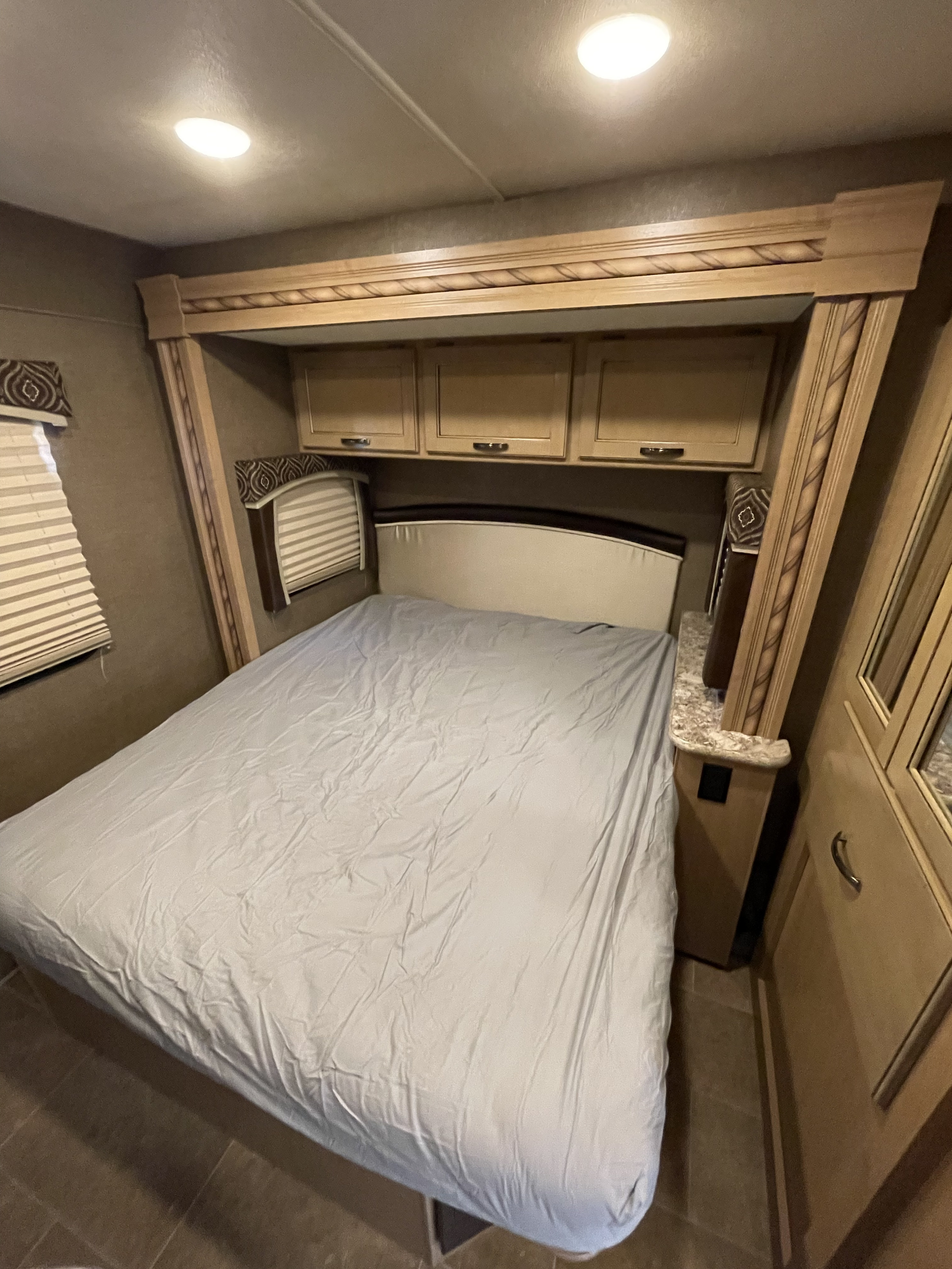 Cozy RV rental bedroom featuring a comfortable bed, overhead cabinets, and window blinds for your travels.. Other Chateau 2018